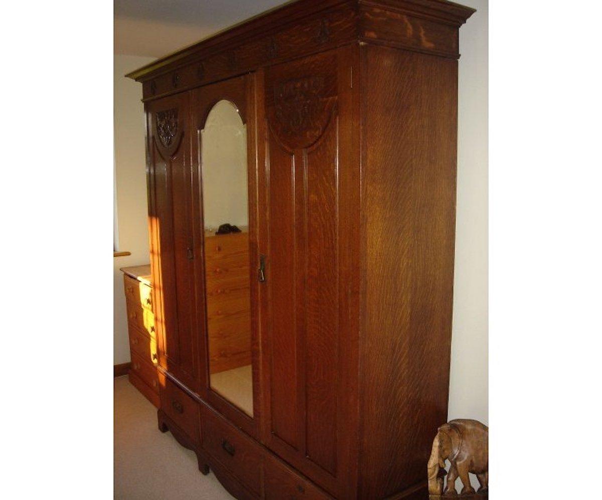 Shapland and Petter. An Arts & Crafts oak treble wardrobe with wild tiger grain throughout, a central beveled mirror door, flanked by two further paneled doors with wonderful stylized floral carvings to the top and below the flaring cornice. The
