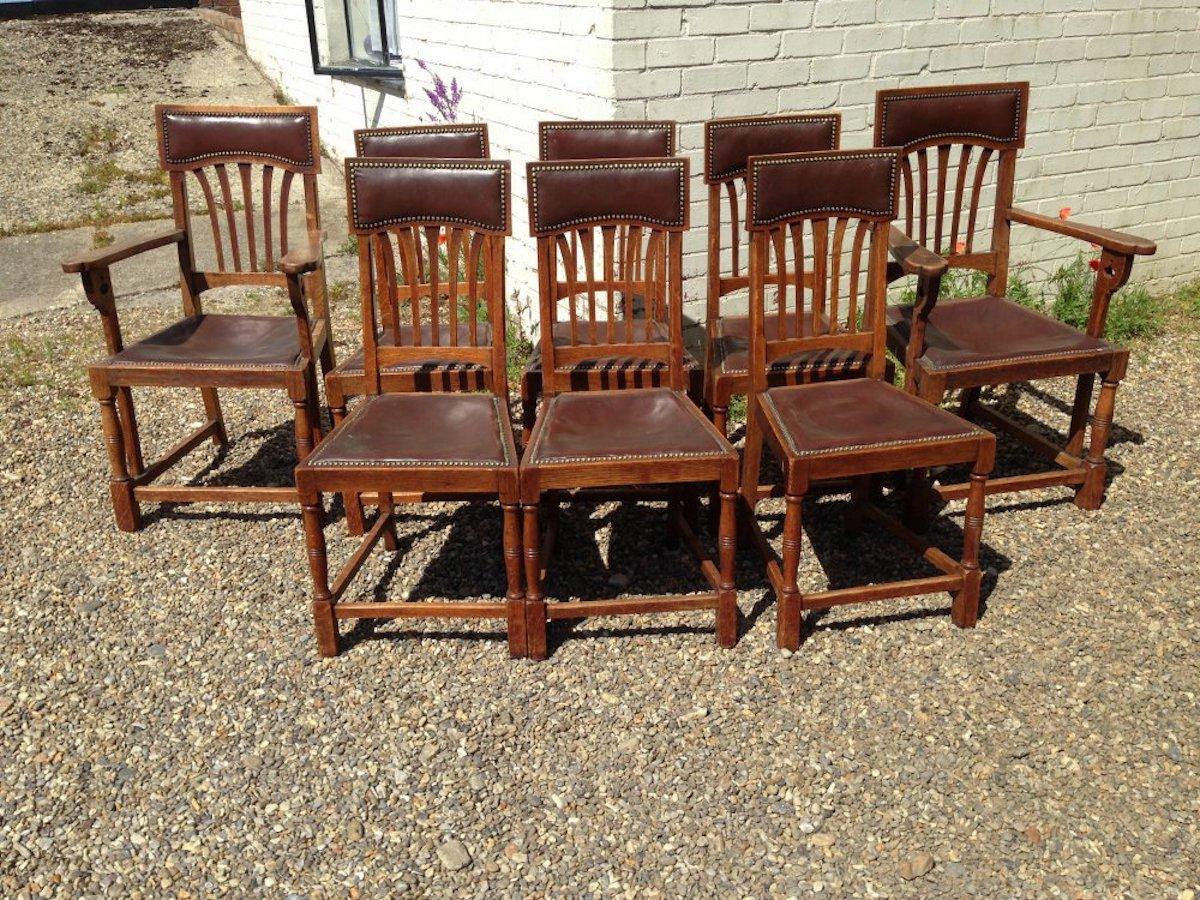Shapland and Petter attributed.
A good set of eight Arts and Crafts oak and leather dining chairs with stylized floral cut-outs to the arms, that follow through to the lower side stretchers making them stronger. 
Armchair measures: Height 42