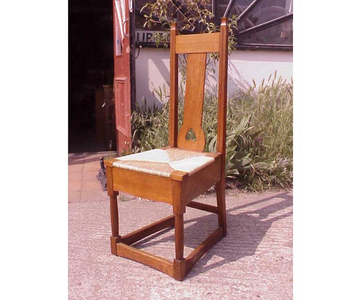Shapland and Petter. A good Arts and Crafts oak rush seated chair in the style of M H Baillie Scott with a lower heart cut-out to the back rest. A wide apron below the seat with subtle shaping to it, turned front legs united by floor stretchers.
