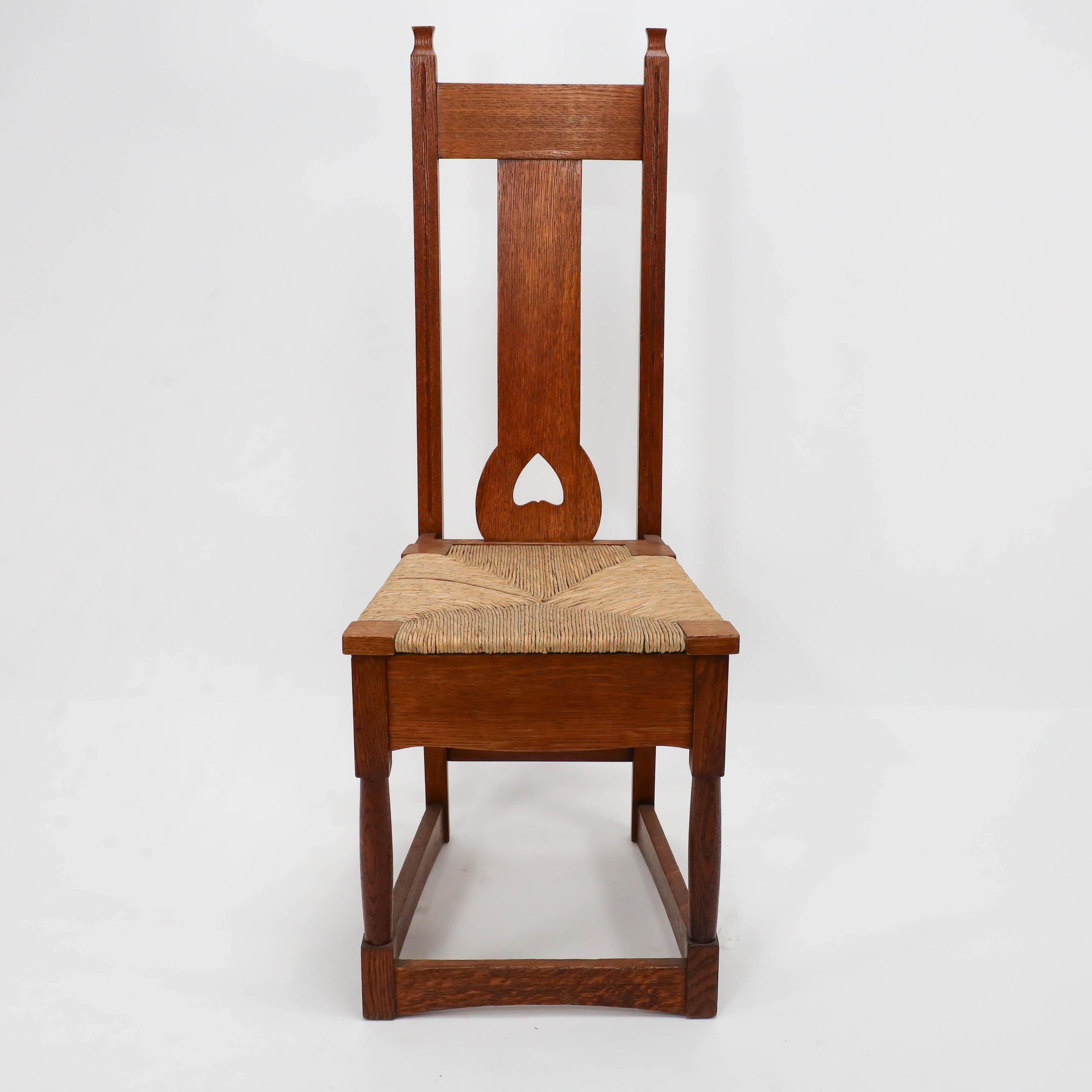 Shapland & Petter. Una buena silla de asiento Arts and Crafts de junco de roble al estilo de M H Baillie Scott, con un corazón recortado en la parte inferior del respaldo. Amplio faldón bajo el asiento, sutilmente perfilado, patas delanteras