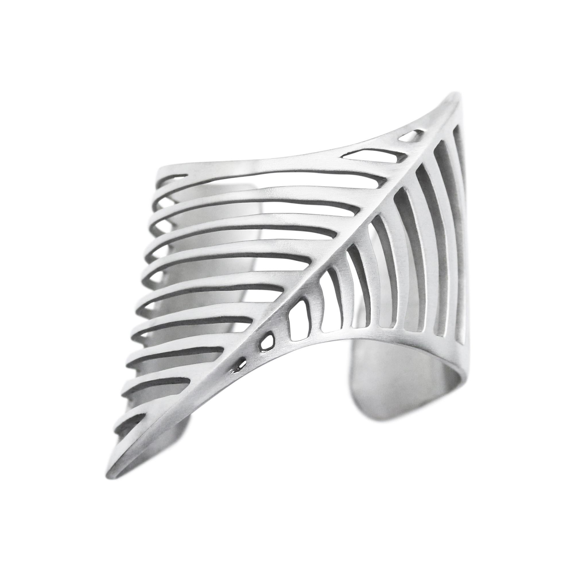 The design is inspired by a fusion of a modernist-futurist architecture from the 1970s and the body of the shark, predator of the ocean. It has cuts in an abstract fishbone pattern.
Shaped to perfectly embrace your wrist. It can be worn as low or as