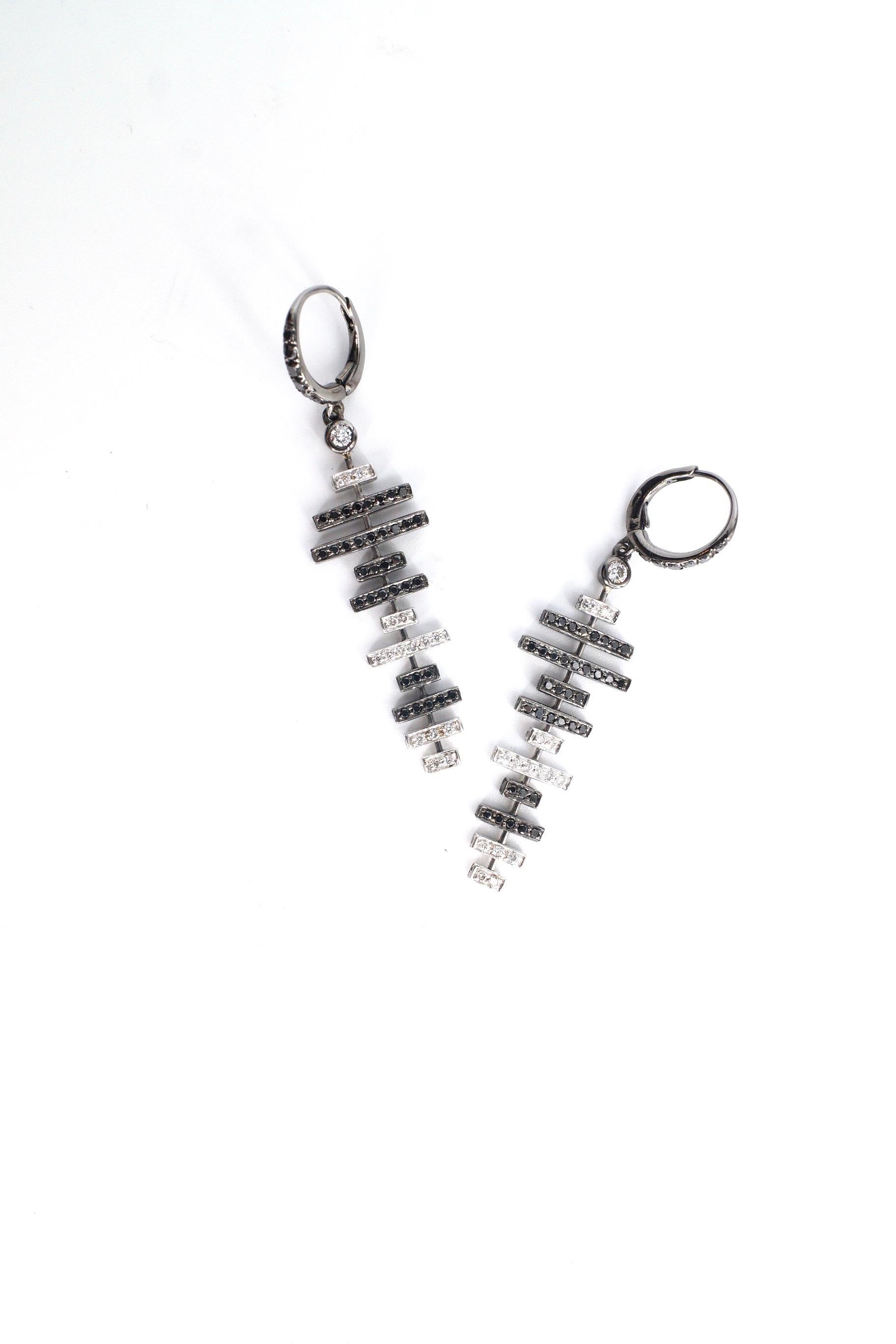 Zyla Earrings
A pair of eighteen-karat blackened white gold vertical earrings, suspended from a black diamond encrusted earwire. Each beginning with a round white diamond, the earrings then consist of eleven horizontal lines of varying sizes, either