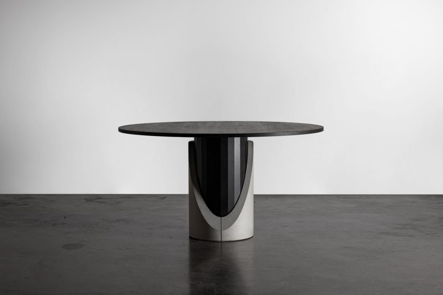 With the Sharp dining table, designer Bertrand Jayr destructures the symbiosis between concrete and metal. The reversible concrete ballast protects and reveals a black metal shaft with delicate facets. The oak veneer tabletop is tinted with a deep