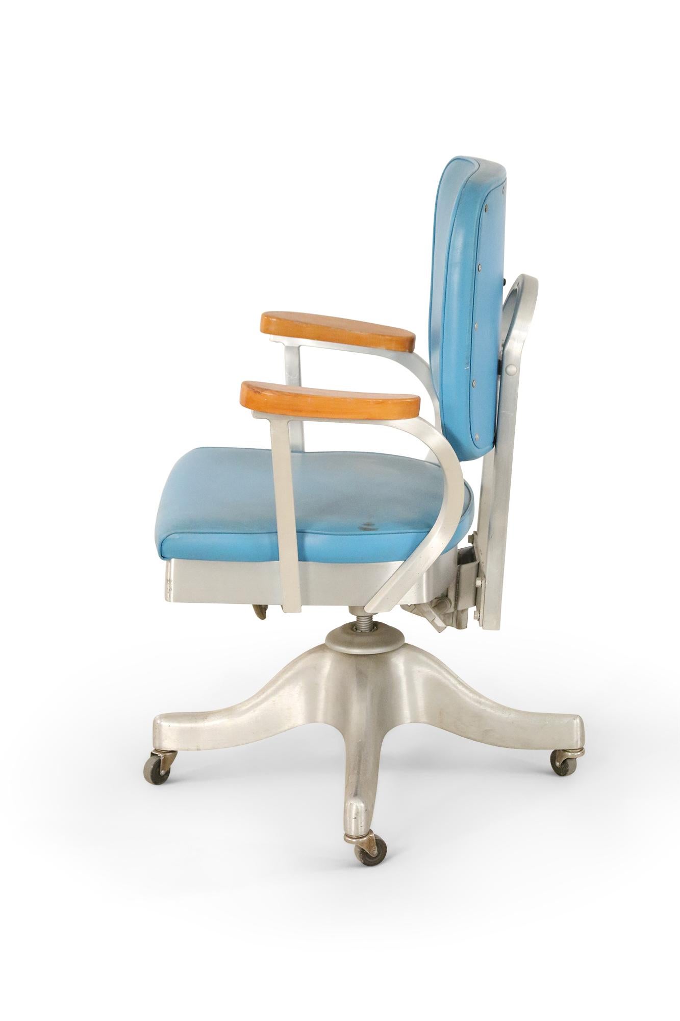 American mid-century rolling adjustable office chair with blue vinyl upholstery, silver metal frame with four wheels, and wooden armrests. (Shaw Walker Co.).
   