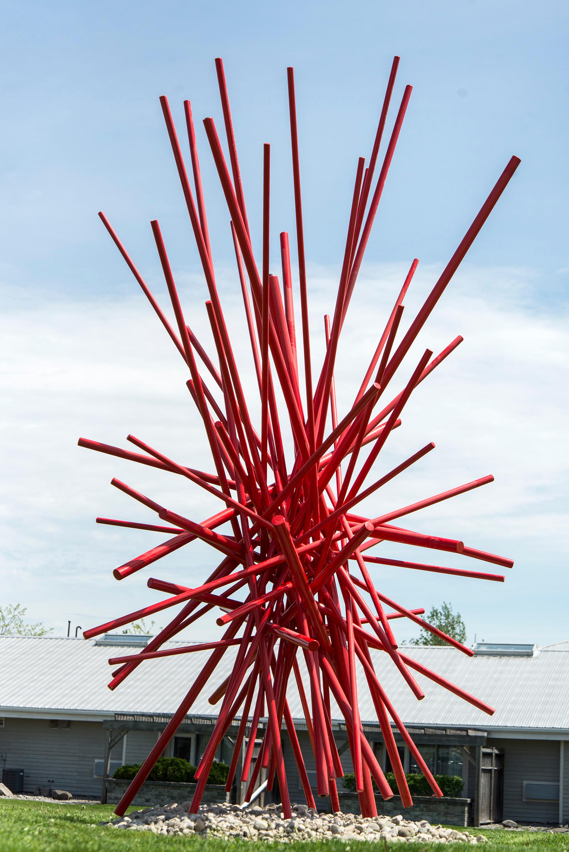 In einer Farbexplosion kreuzen sich leuchtend rot lackierte Stahlstangen in dieser dynamischen abstrakten Skulptur von Shayne Dark. In seinem Studio auf dem Lande lässt sich der kanadische Künstler ständig von der Natur inspirieren. Durch die