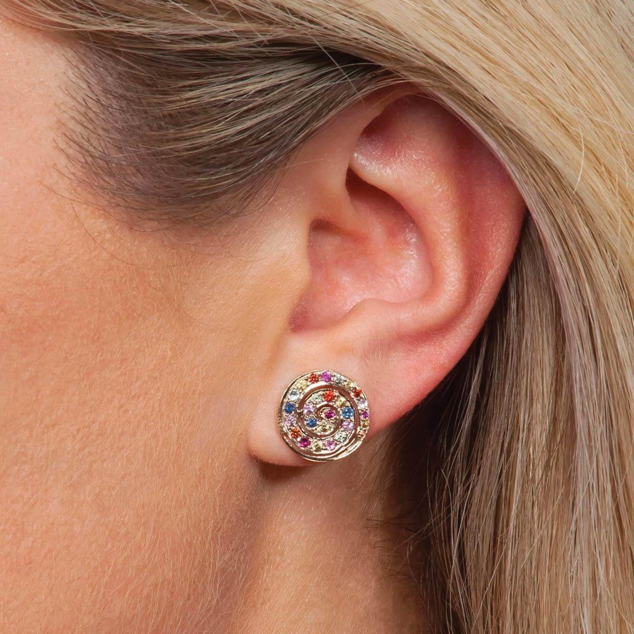 An unexpected and elegant twist on classic studs, these button earrings are enhanced with a rainbow swirl of colored gems. 14k yellow gold with sapphire, tsavorite, amethyst and blue topaz. 0.51” diameter.



