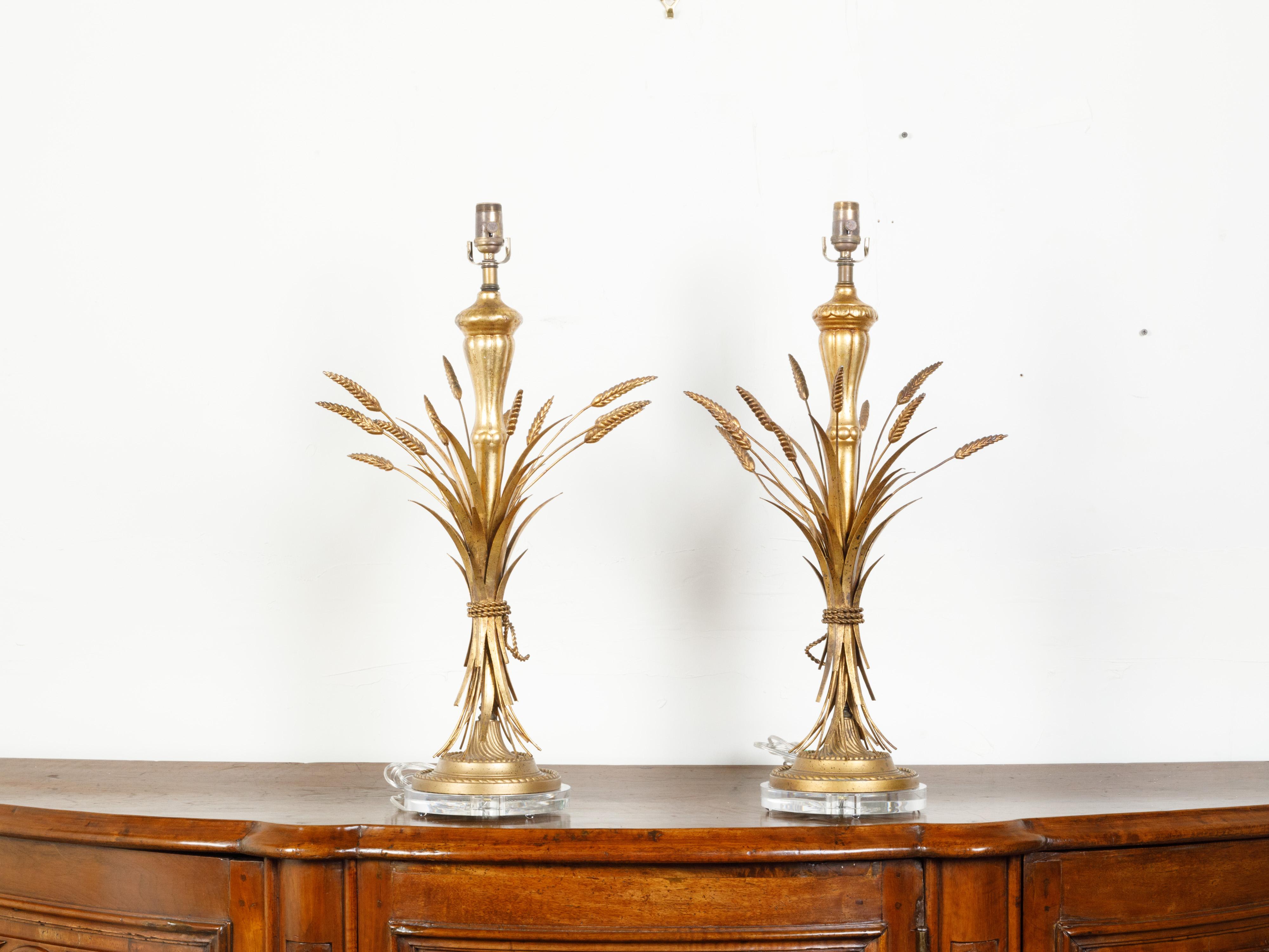 A pair of gilt metal table lamps from the mid 20th century, depicting a sheaf of wheat on lucite bases. Created during the mid-century period, each of this pair of gilt metal table lamps, professionally rewired for the US, captures our attention