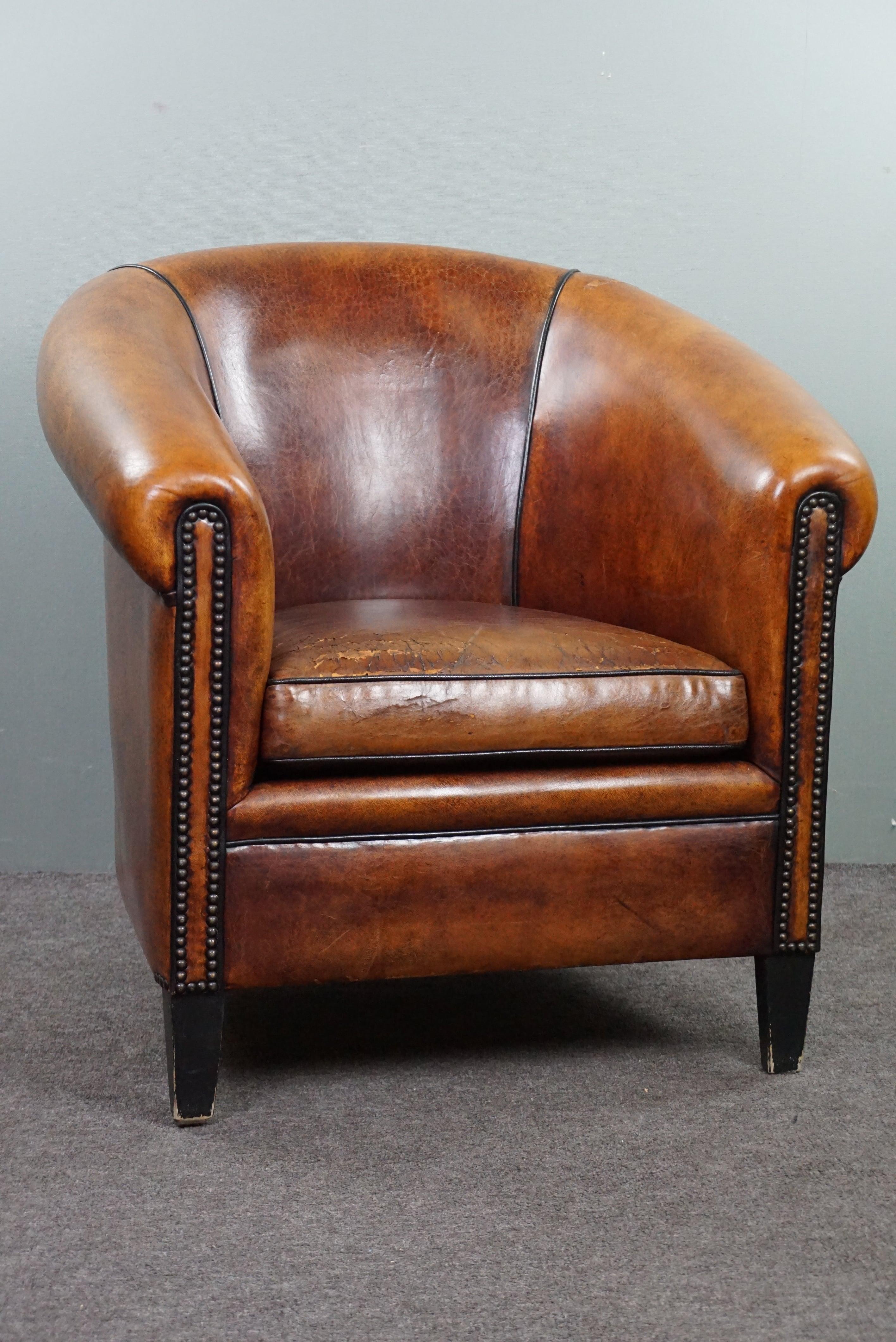 With pride we offer you this beautiful sheep leather club armchair.

This well-crafted club armchair exudes a robust appearance, making it a true centerpiece in almost any interior. The shape, patina, nailhead detailing, and color of this club