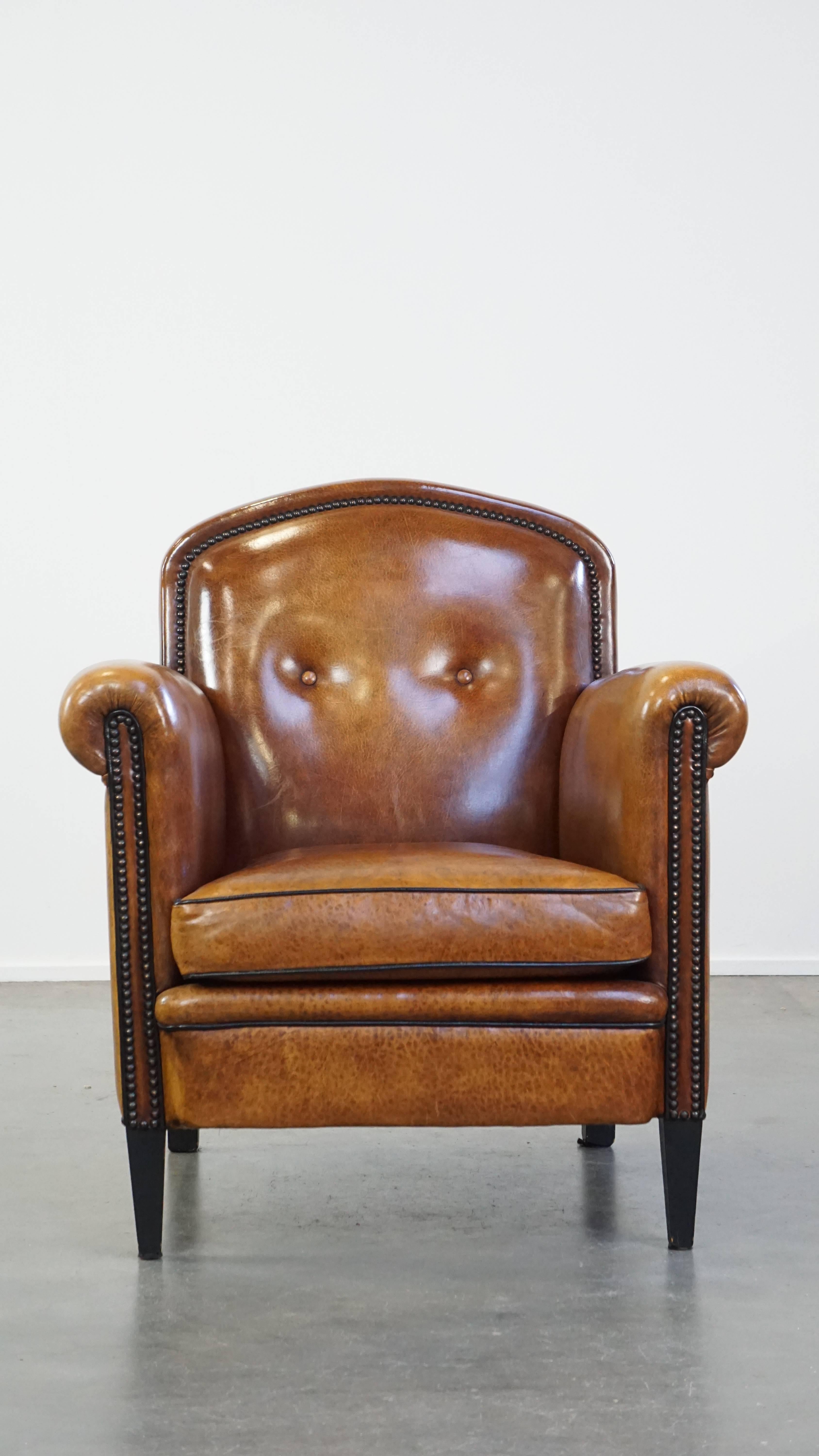 This warmly colored, well-maintained sheepskin leather armchair has a beautiful natural patina and is beautifully finished with decorative nails and black piping. It will complement virtually any space perfectly. The armchair features a removable