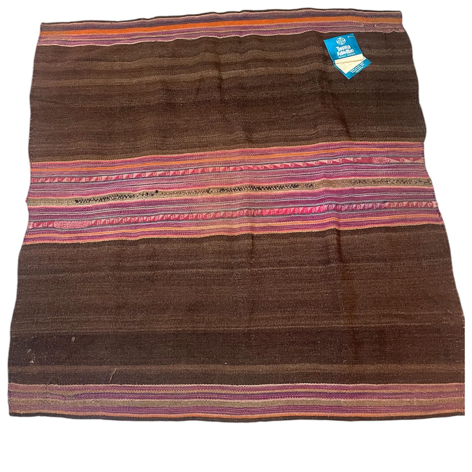 This hand-woven blanket is made from sheep's wool and features a deep black base and multicolored earth-toned patterns. The intricate details feature traditional geometric motifs from the culture, capturing the essence of life and nature in the