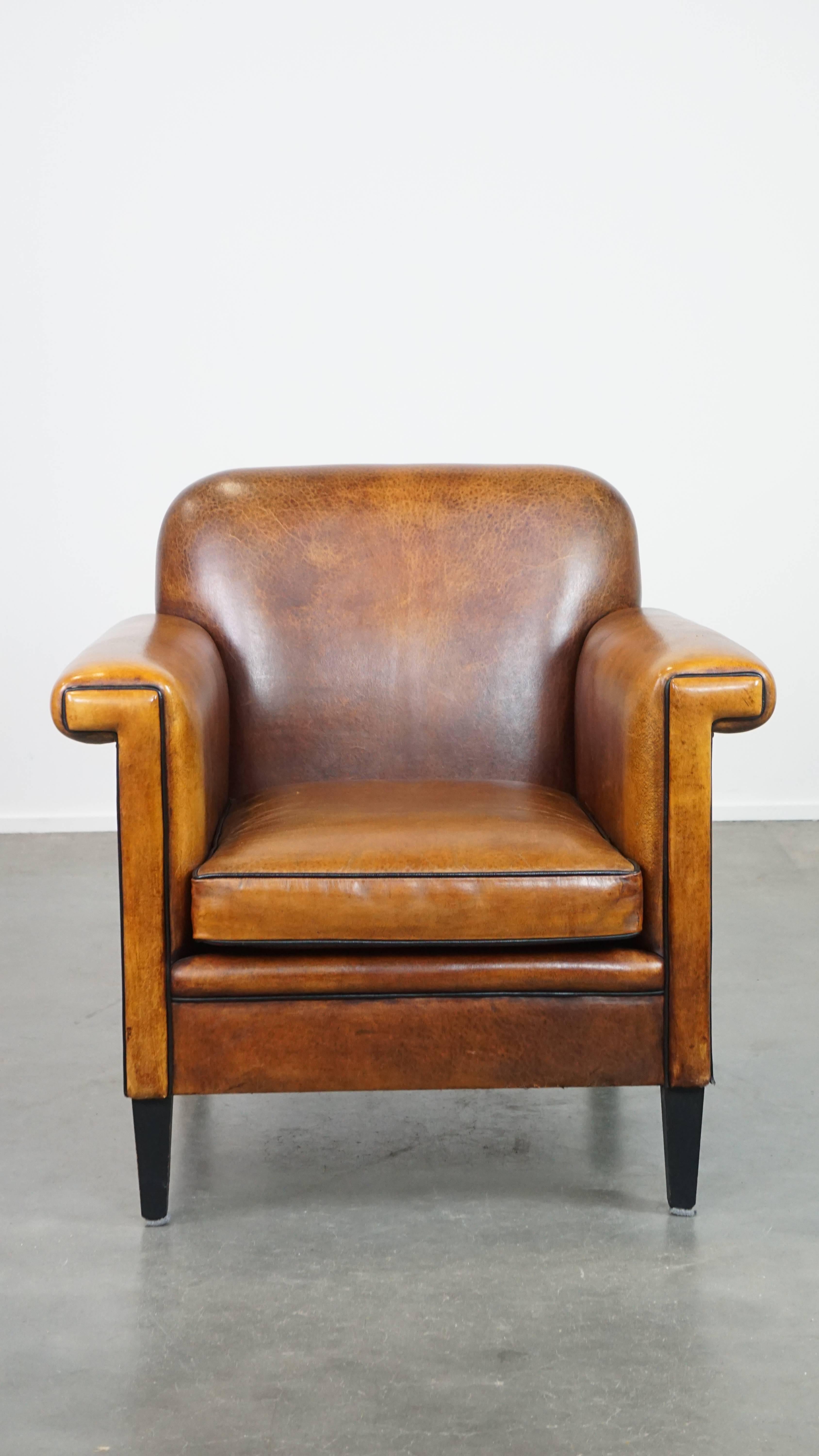Dieser schöne Schafsledersessel greift die eleganten, geometrischen und fast mechanischen Formen auf, die für das Art-Déco-Design charakteristisch sind. Sie ist mit schwarzen Paspeln versehen und weist charmante Details auf. Der Sessel ist mit einem