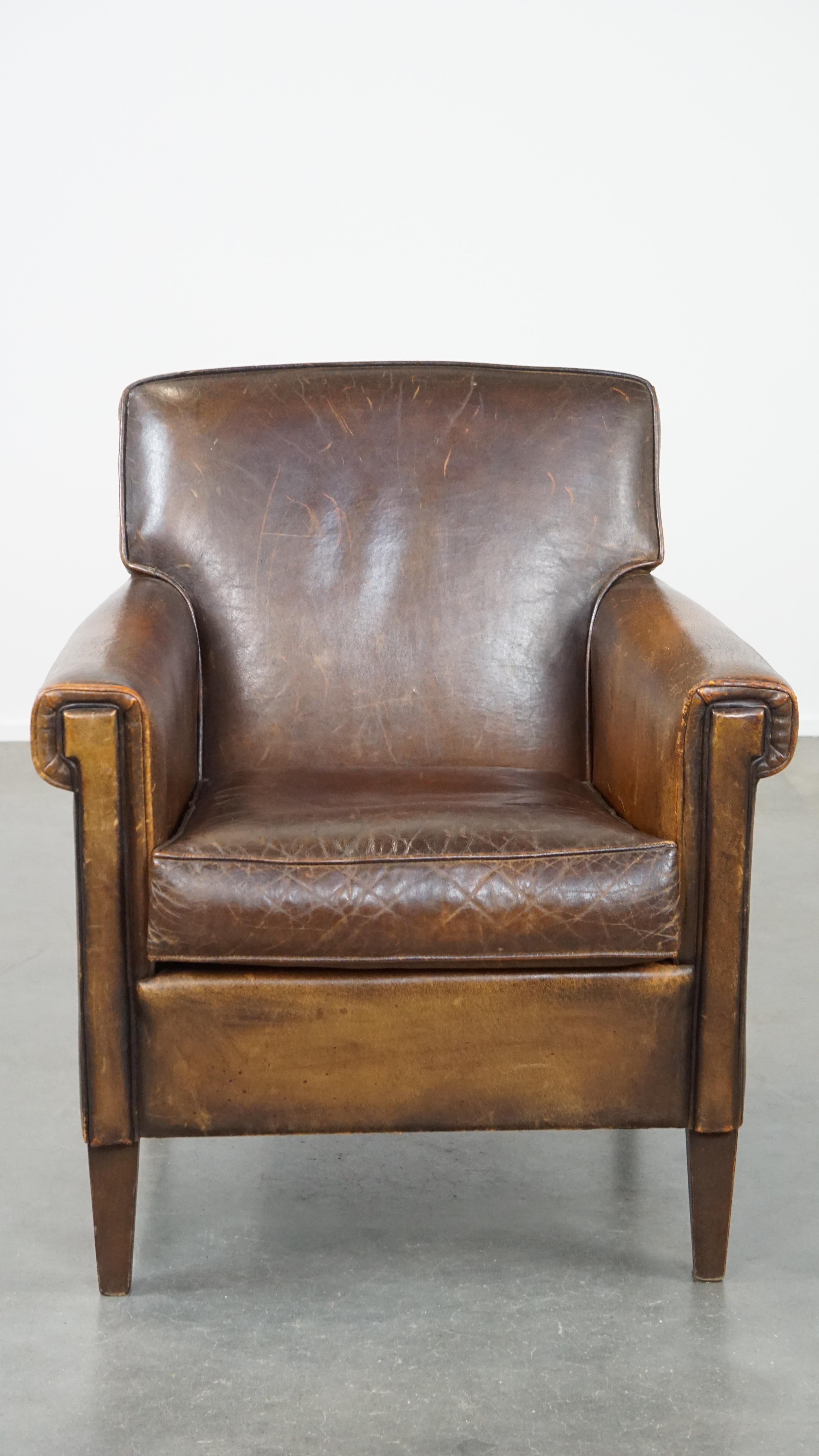 Ce fantastique fauteuil en peau de mouton, malgré sa taille subtile, a un caractère robuste et saisissant. Ses couleurs sombres et ses lignes droites et épurées lui confèrent également une touche de design Art déco. Le fauteuil est doté d'un coussin