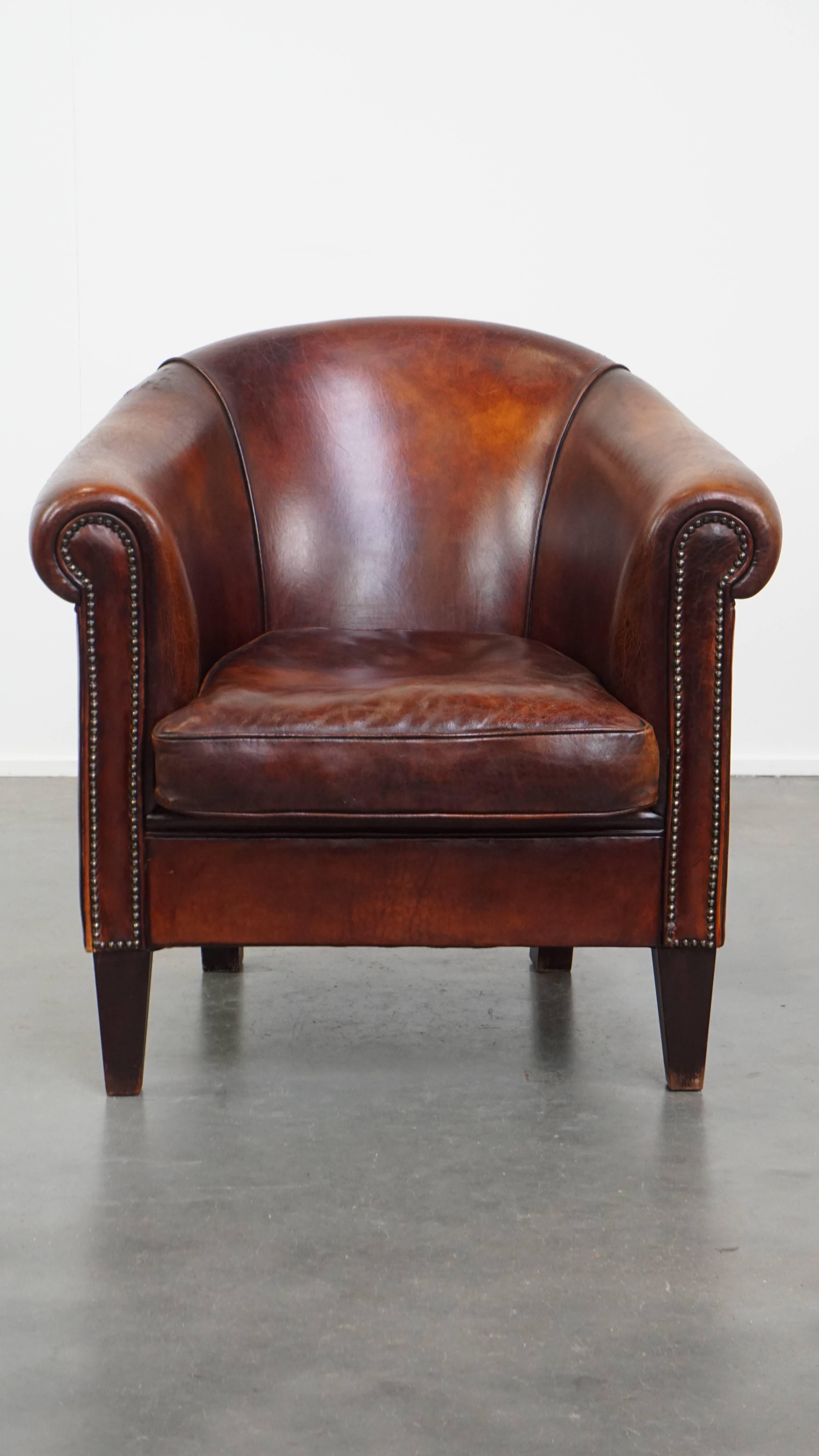 Questa sedia da club in pelle di pecora è di un bel colore cognac caldo con una bella patina. Questa sedia ha un aspetto ricco e invitante grazie alle sue tonalità calde e profonde. Nel corso degli anni ha sviluppato una splendida patina che ne