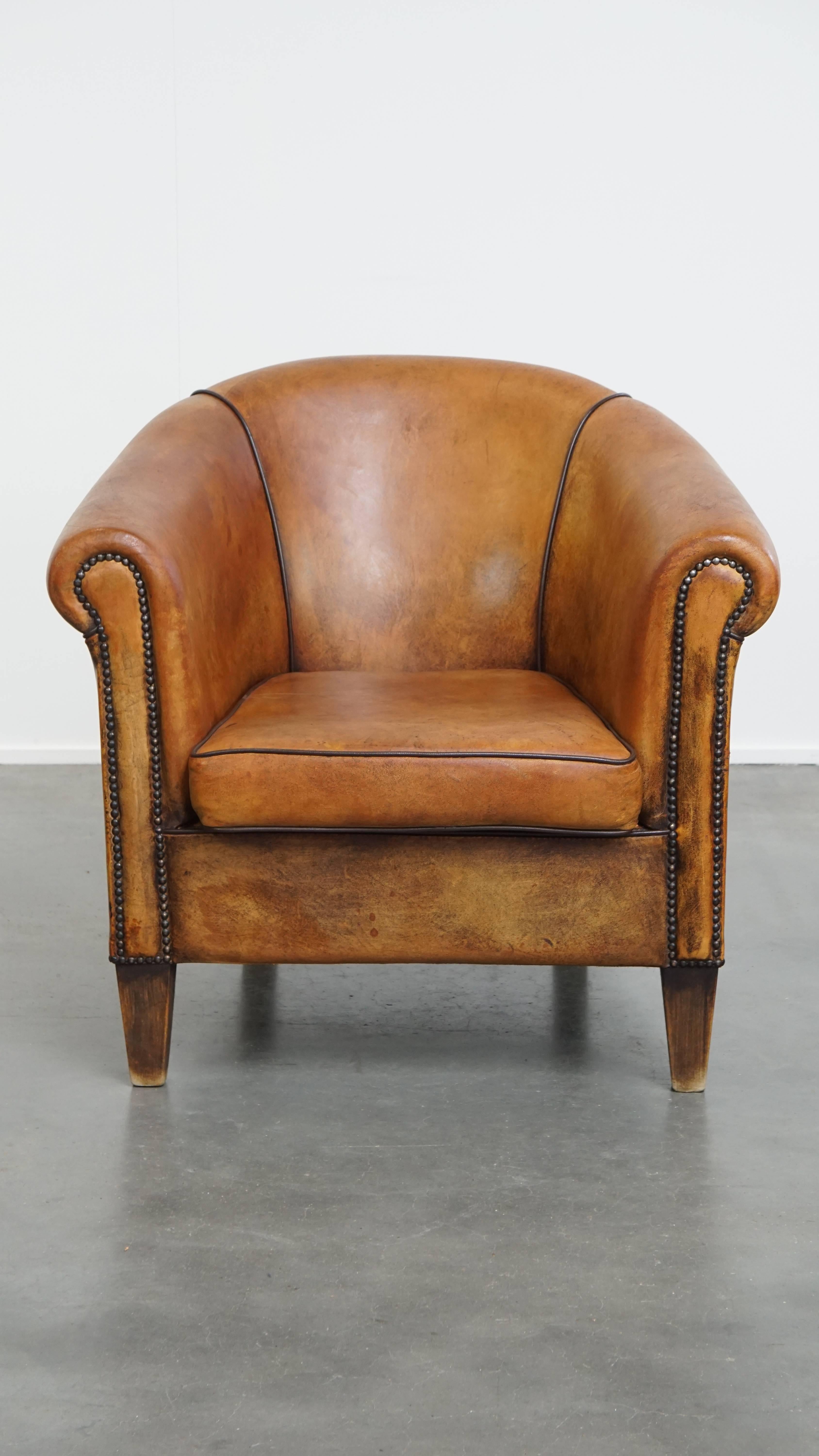 Offered is this sheepskin leather club armchair in English style, full of character and boasting a beautiful patina. 

This armchair features a loose seat cushion and provides excellent and supportive seating comfort. It is beautifully finished with