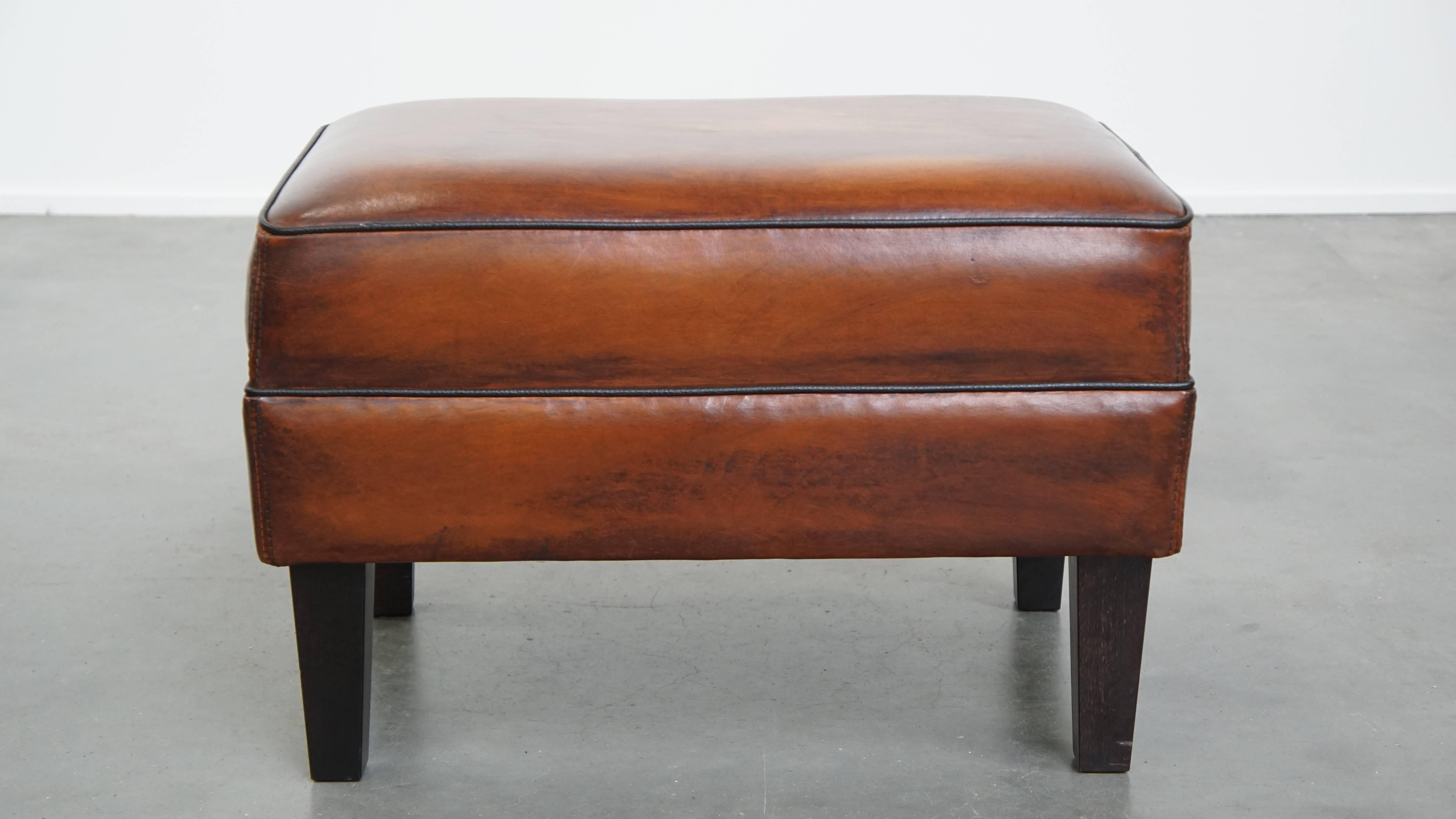 Angeboten wird hier ein Schafsleder-Ottoman in ausgezeichnetem Zustand, mit schwarzem Keder versehen. Ein Schafsfellhocker, auch Ottomane genannt, verwandelt Ihren ohnehin schon bequemen Sessel in ein wahres Entspannungsparadies. Wenn Sie Ihre Füße