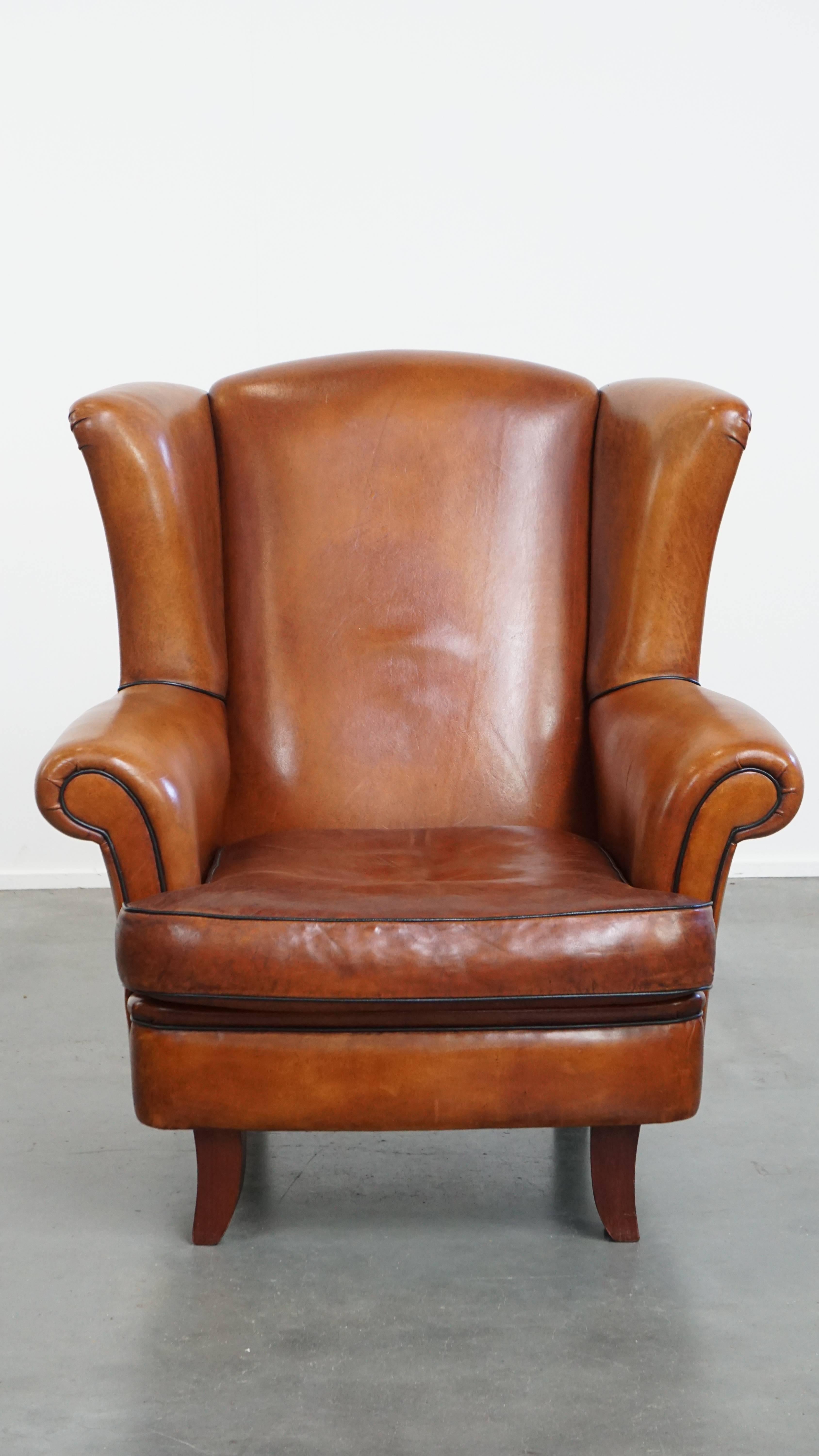 Nous vous proposons cet élégant et généreux fauteuil à oreilles en peau de mouton aux tons chauds et à la finition raffinée avec des passepoils noirs. 

La chaise présente un design gracieux et est finie avec des garnitures noires distinctives. Il