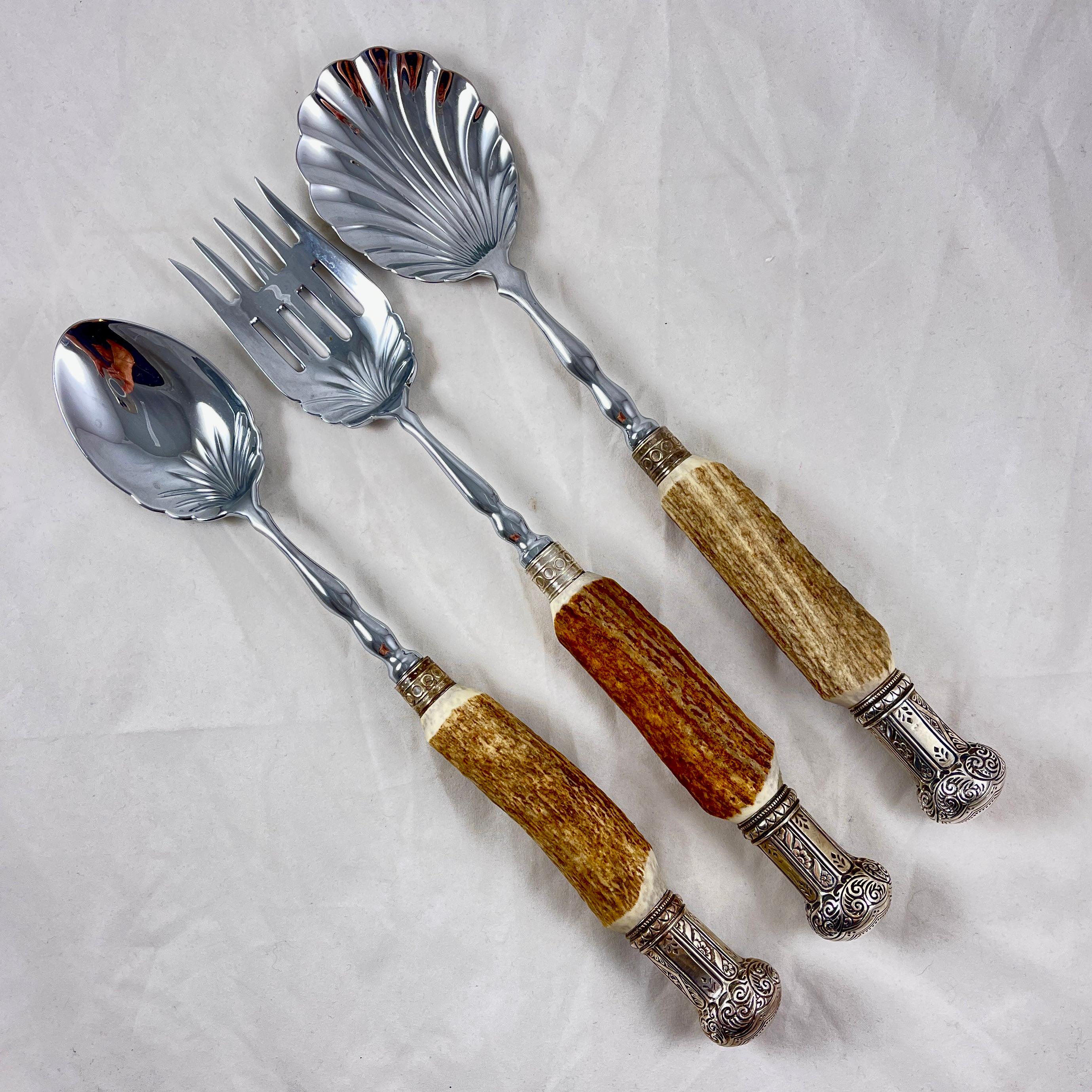 A three piece serving set with Stag Antler handles and Sterling Silver ferrules and end caps, Sheffield, England, circa mid 20th Century.

Impressively sized, the set consists of a scalloped bowl spoon, and a spoon and fork of a similar pattern,