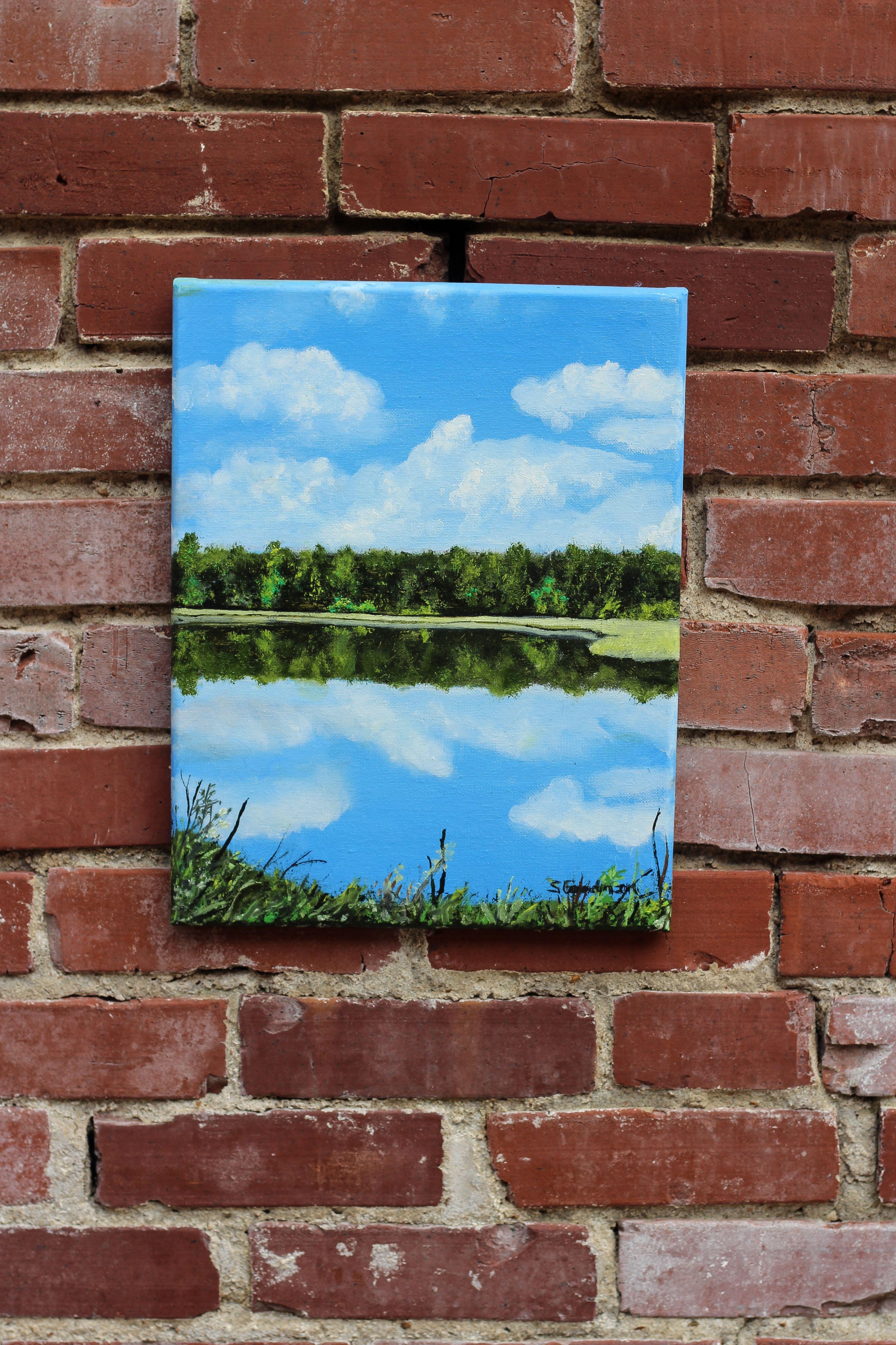 <p>Kommentare der Künstlerin<br>Die Künstlerin Shela Goodman zeigt einen ruhigen Blick auf einen Fluss mit üppiger Vegetation. Wolken und Bäume reihen sich aneinander und spiegeln sich im Wasser, während das Blattwerk den unteren Teil der Szene