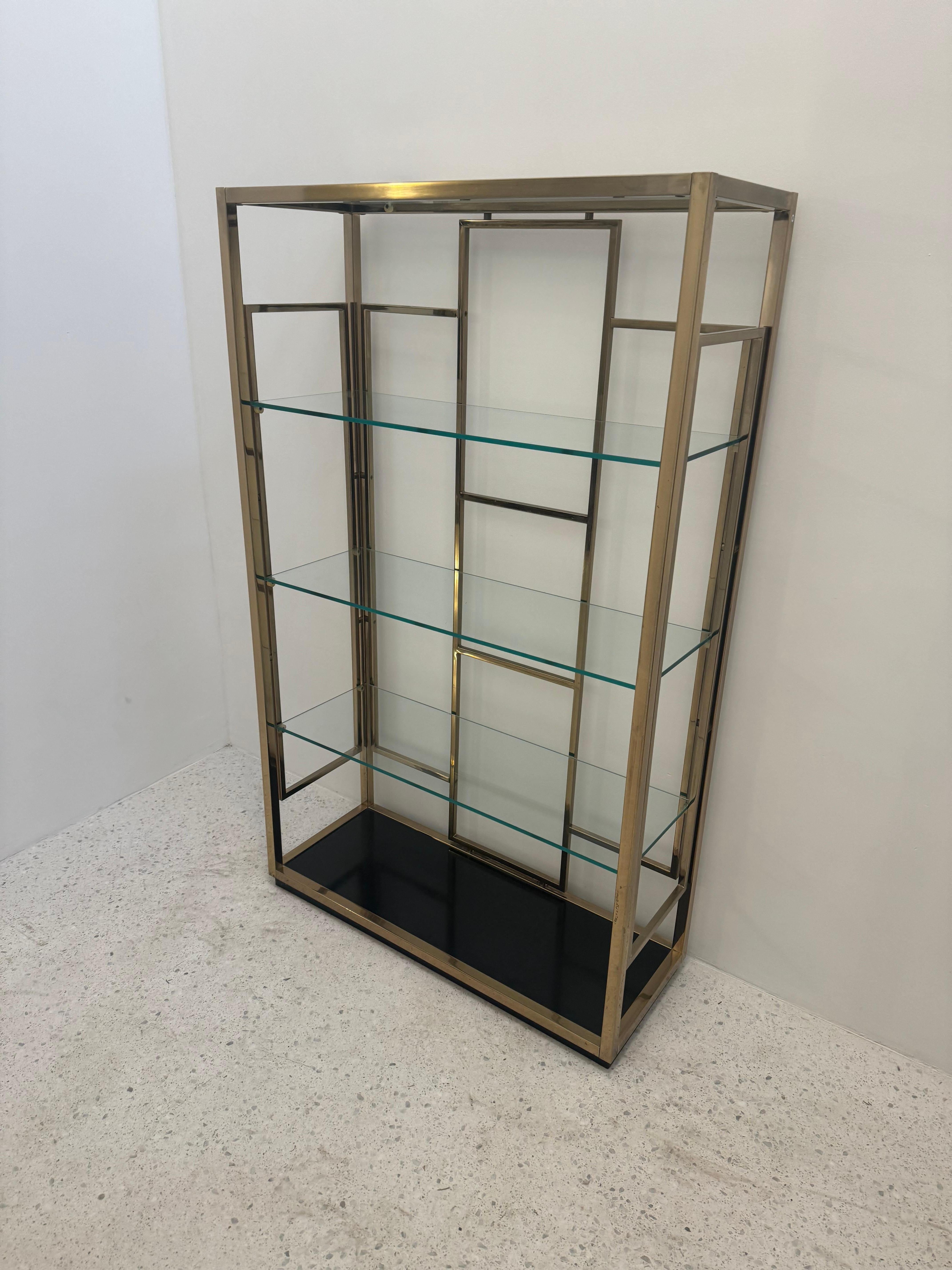 Shelf with a gilded metal structure made up of rectangular panels and three glass shelves.
