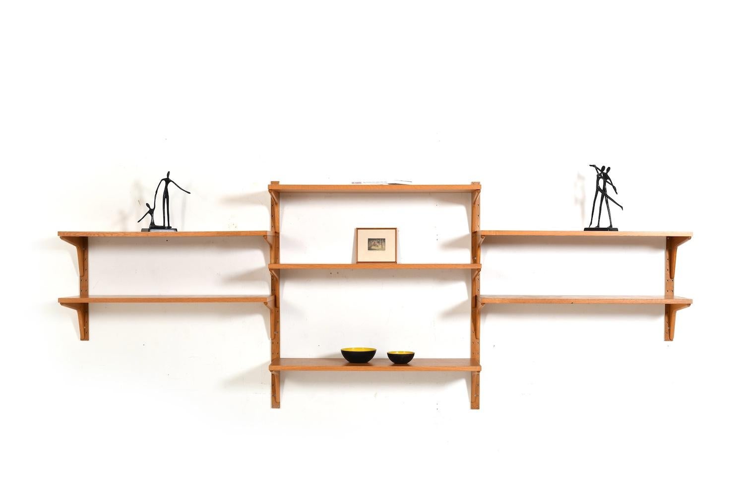 Regalsystem aus Eiche von HG Furniture Dänemark 1960er Jahre.
Die Schrankwand besteht aus:
- 7 Einlegeböden
- 4 Wandhalterungen

detaillierte Messungen:
Regale: 7x  89,5 cm x 30 cm (B x T), Höhe Wandhalterungen: 2x 102 cm, 2x kleinere