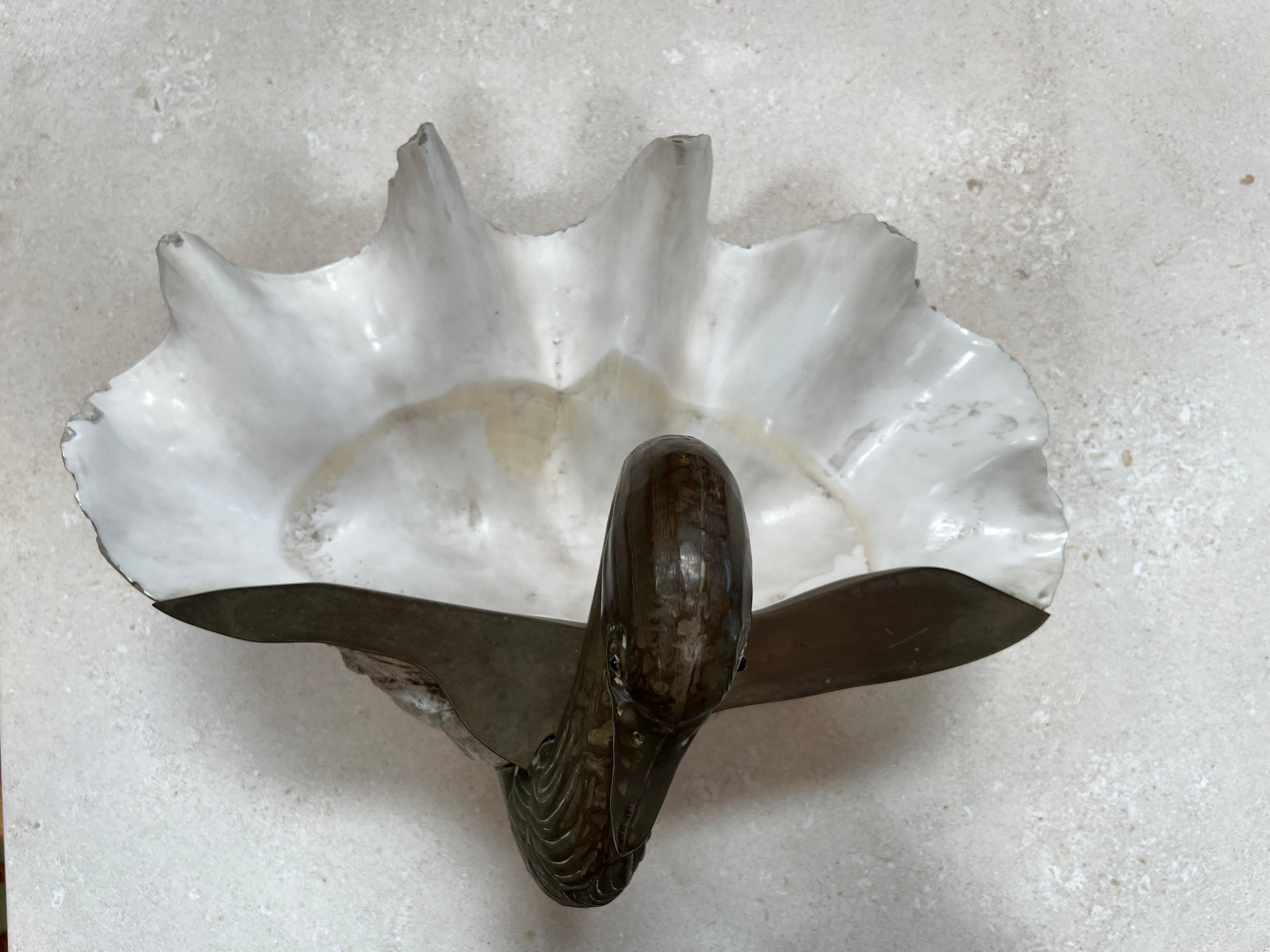 The Shell and Silvered Brass Duck Shaped Trinket-Bowl, crafted in Italy circa 1970, is a charming and whimsical piece of art. Its unique design features a delicate shell serving as the bowl, beautifully complemented by silvered brass detailing in