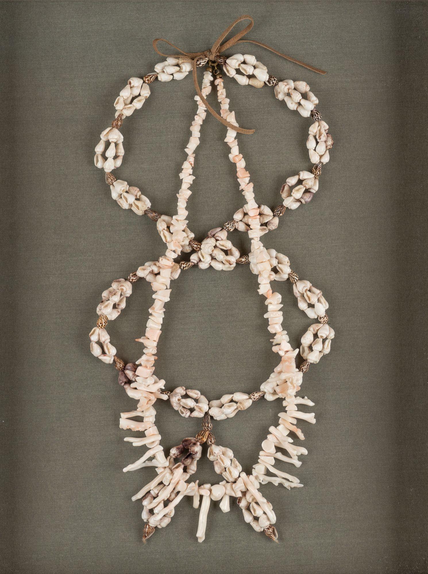 Threaded cluster of shell and white branch coral necklaces mounted on a green linen backing in a shadow box frame.