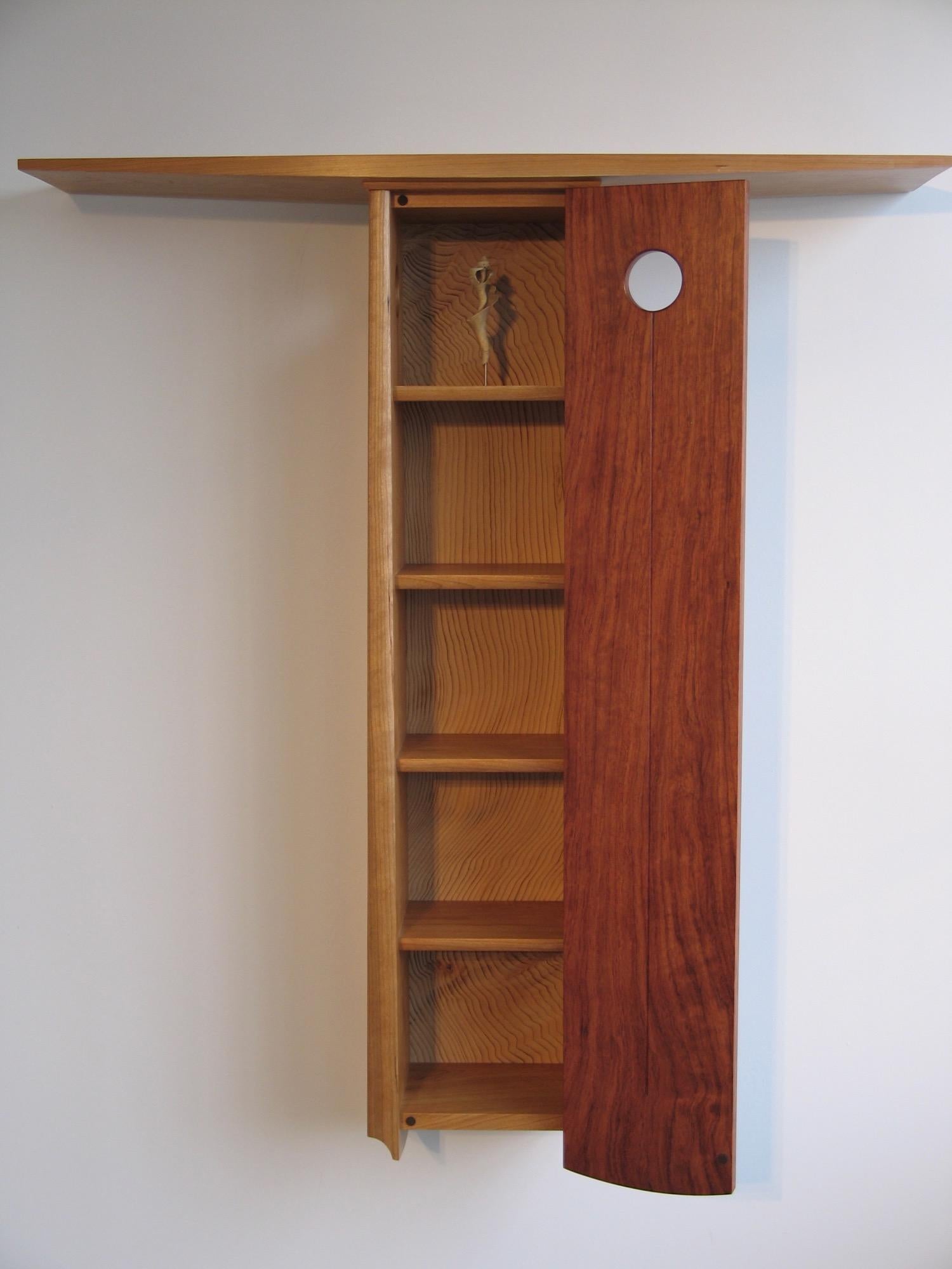 Rocky Point,  a wall hung cabinet of curiosity. 

A glimpse of the shell through the port hole in the figured bubinga door that beckons to be opened, revealing the shell and added treasures against the intense grain and intoxicating scent of cedar