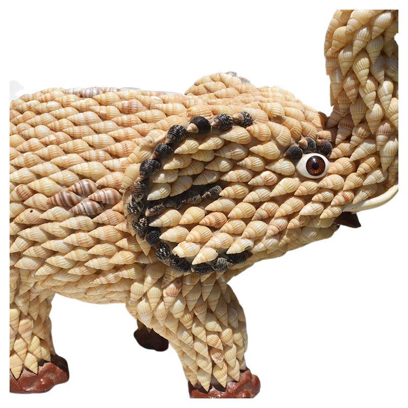 A large tall lucky sea shell encrusted elephant statue or figurine. Covered in shells, this elephant stands with its trunk up pointed toward the sky. In Southeast Asia, elephants with trunks that point upwards, are known to be good luck. It is