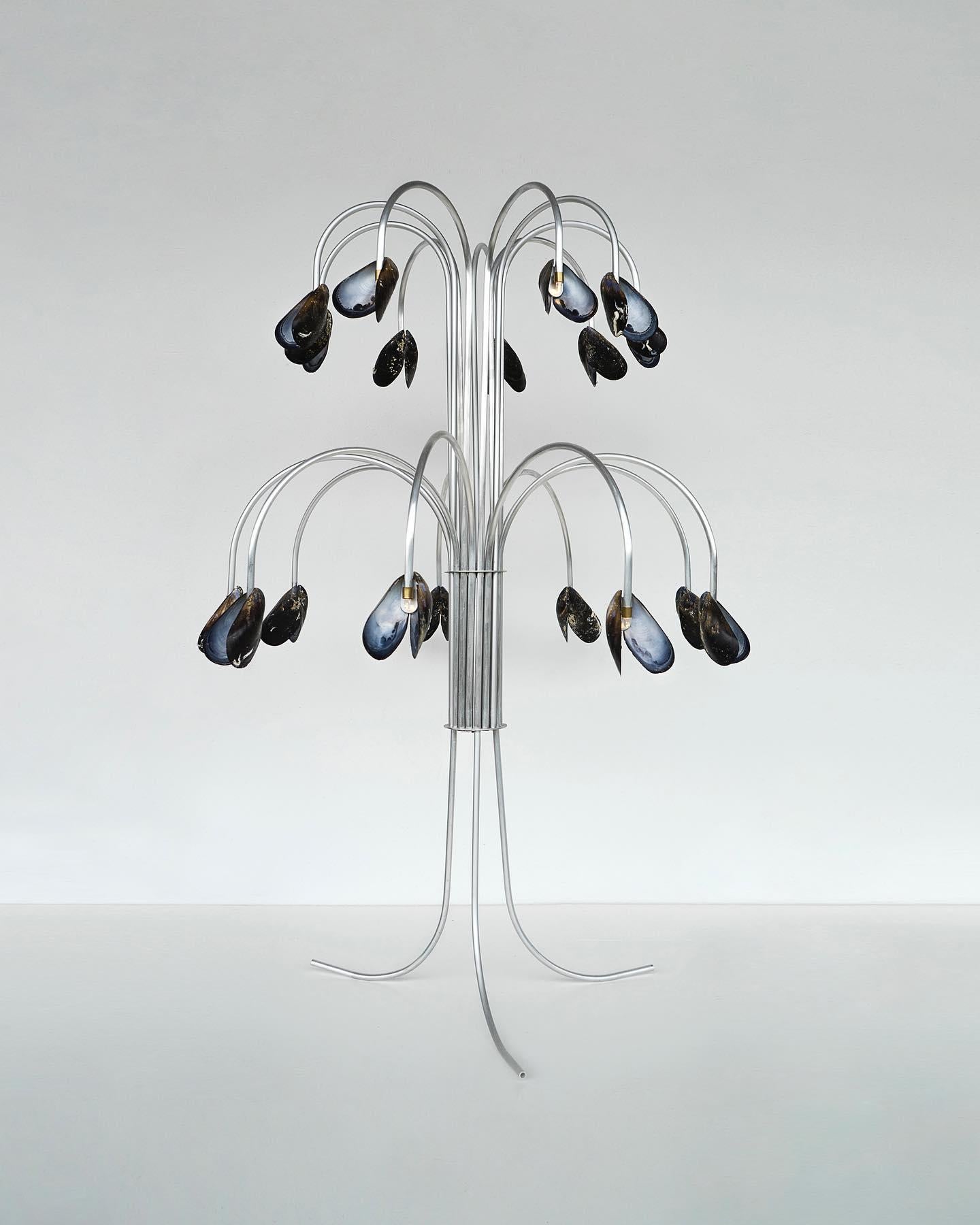 Shell Light by Touch With Eyes
Dimensions: W 50 x D 50 x H 70 cm
Materials: Metal- aluminum, mussels. 
Weight: 3 Kg. 

The light was made with shells founded on beaches. Moving around Europe in the car in which Touch With Eyes set up their workshop,