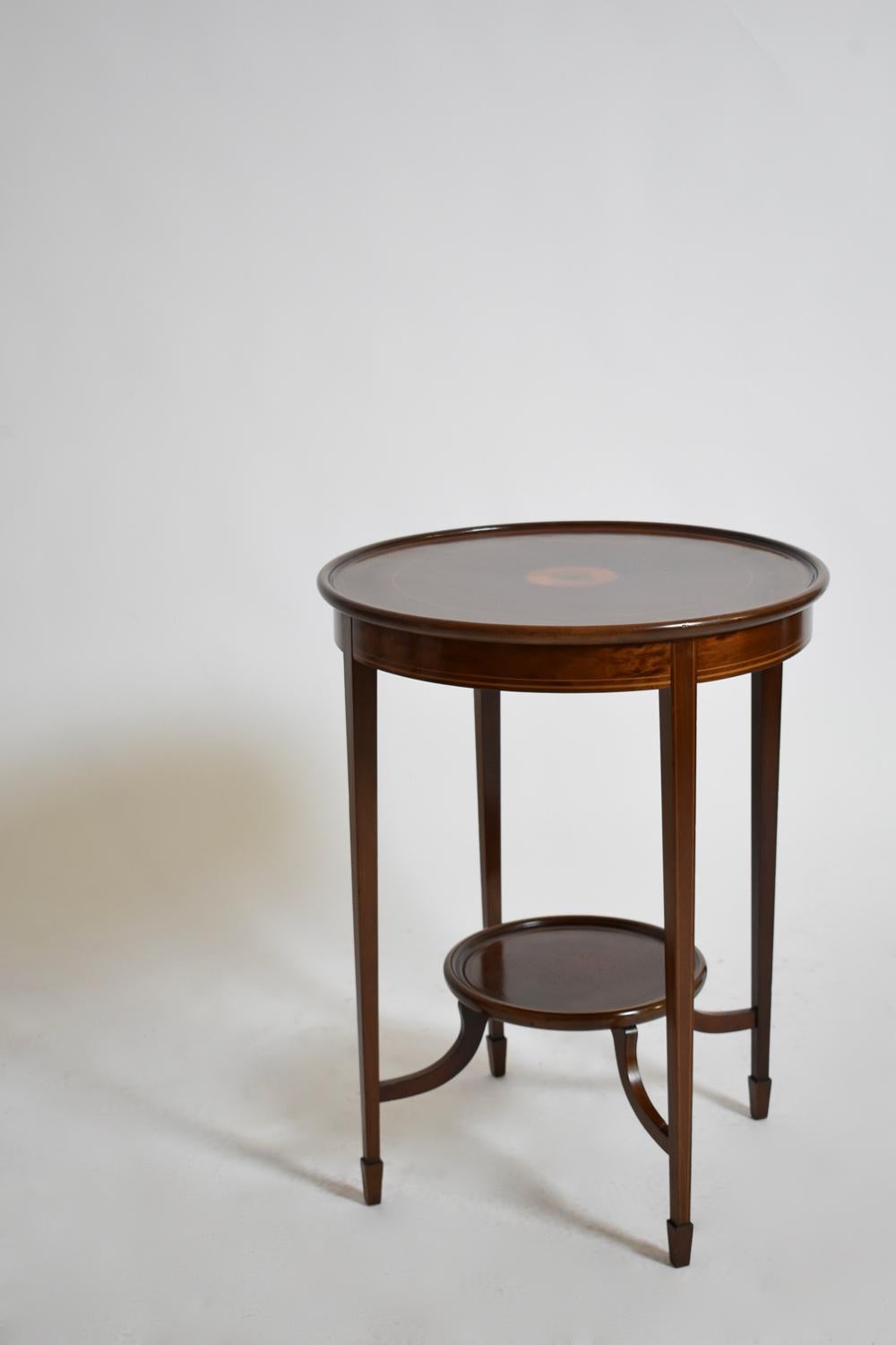 Guéridon rond en placage d'acajou et filets de bois clair avec décor de coquillages incrustés. Repose sur quatre pieds reliés par une table à tête cruciforme. Angleterre, C.I.C.