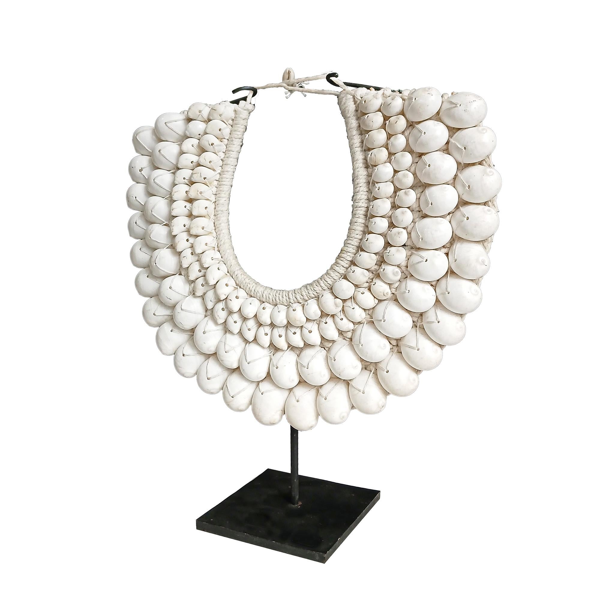 A male necklace from the Asmat Village, Papua New Guinea.

Four rows of large polished white cowrie shells in two sizes, seamlessly sewn onto a cotton macramé base, which has been hand-knotted around a semi-circular bamboo frame. A money cowrie