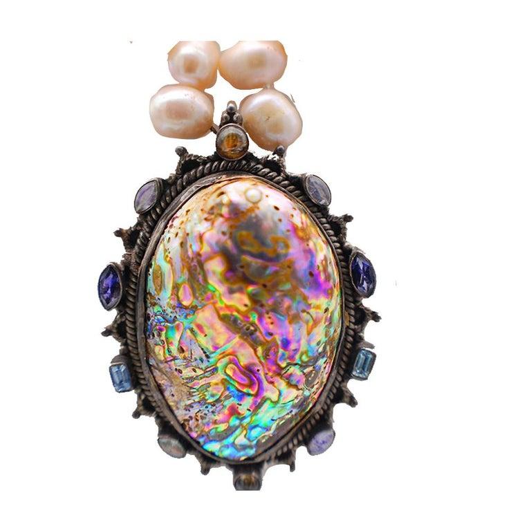 Abalone large shell with natural colorful array is adorned with surrounding gemstones and suspended on a strand of pink Biwa pearls.
Gemstones include Aquamarine and Sapphires all natural set around pendant.
Spectacular, large pendant measures 3 x 2