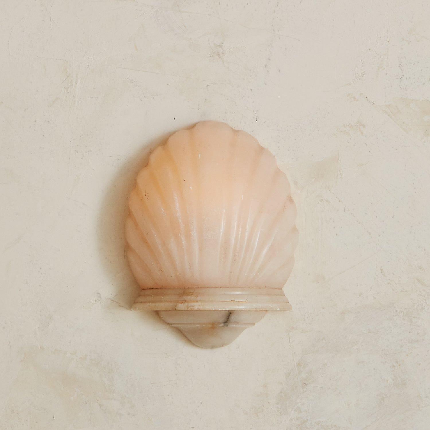 A gorgeous shell sconce carved from alabaster. When lit, this sconce emits a warm light that highlights the natural veining of the stone. ‘1922’ carved on the inner base. Sourced in France.