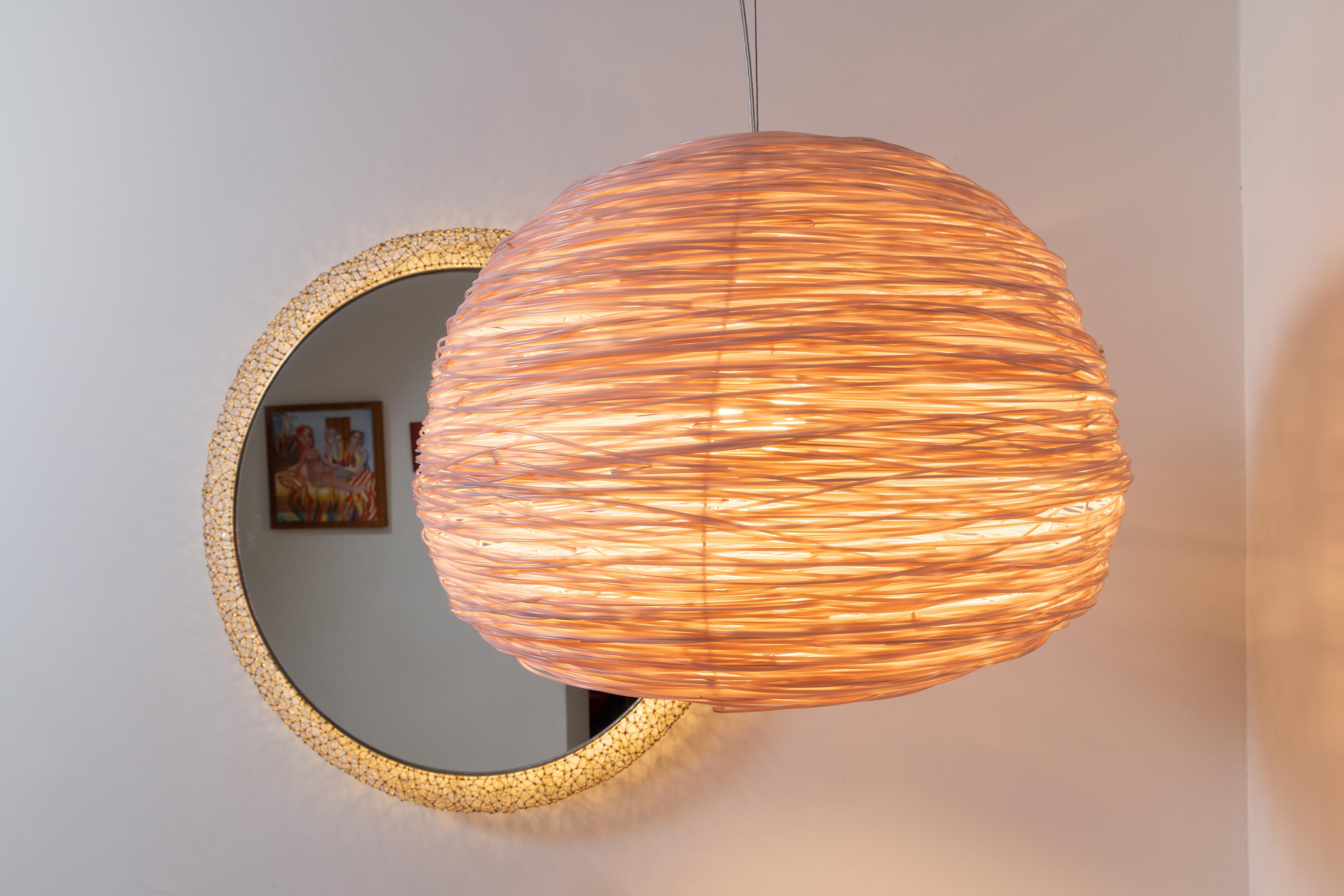 Shelter pendant in Pink is created with the elemental and universal form of a loosely woven nest like home, this is then incarnated by the light inside, which diffuses through many metres of lateral recycled plastic waste material 

The Shelter