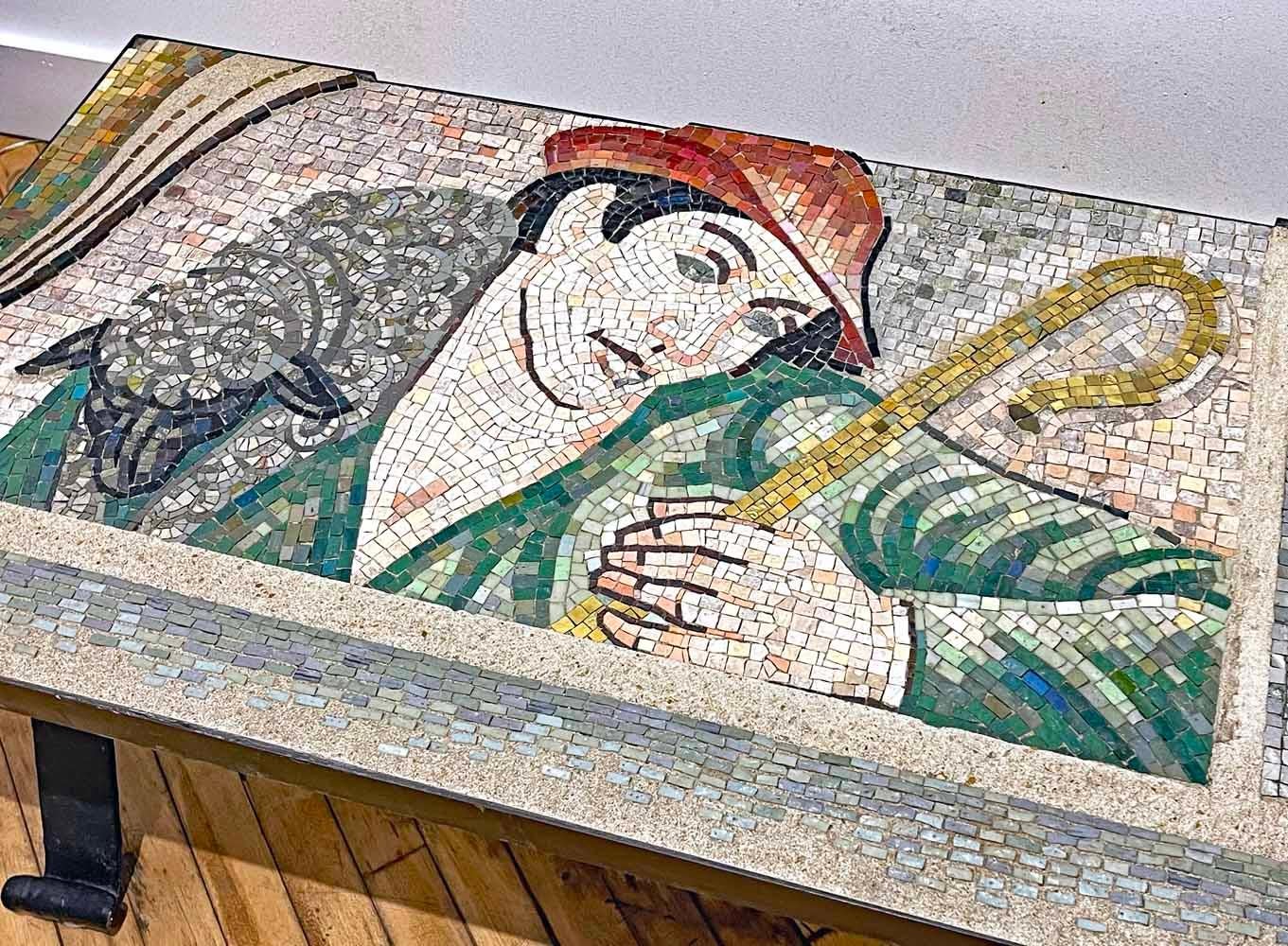 This stunning Art Deco table depicting a shepherd with a sheep over his shoulders, with a golden crook in his hand, is a tour de force of mosaic artisanry.  The artist has used tesserae in stone and glass in tones of deep red, forest green, bright