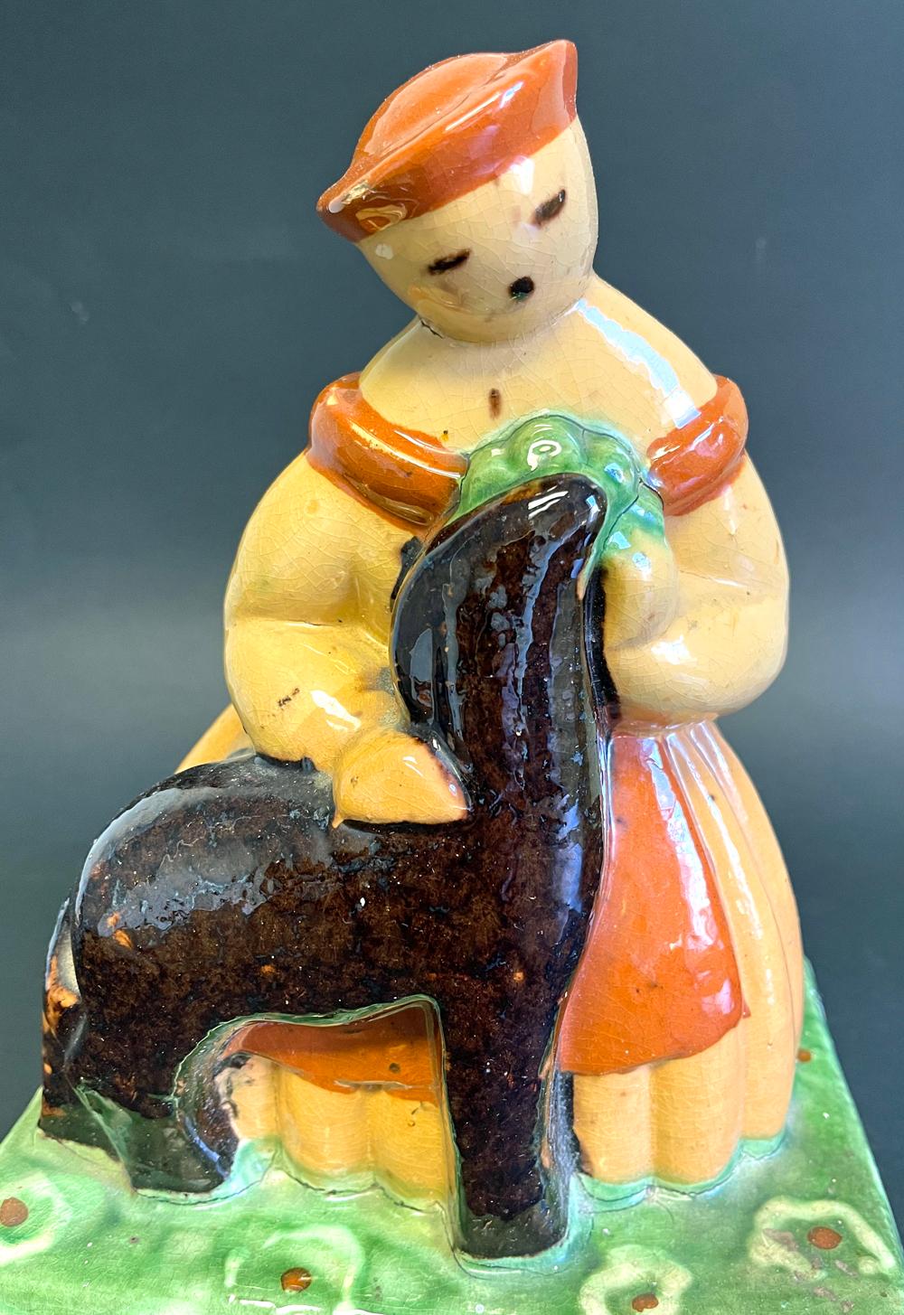 Brilliantly glazed in hues of dark pumpkin, emerald green and ruddy putty, this unique ceramic sculpture of a shepherdess in a wide, pleated skirt embracing one of her lambs was created by the famed Primavera workshop, established by Le Printemps