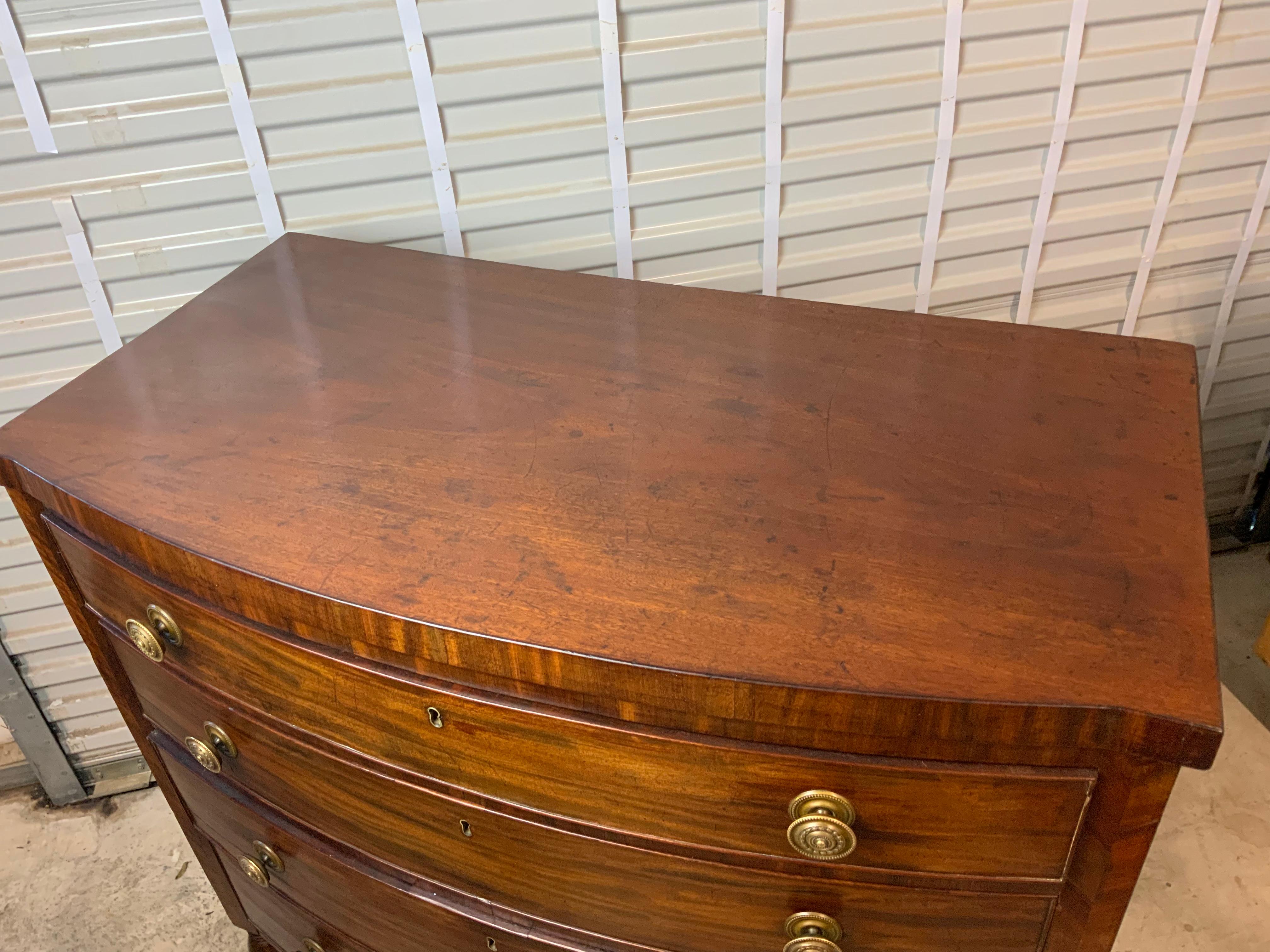 A very nice American Sheraton Mahogany bow front chest 1820-30. Four graduated drawers working smoothly with the original locks intact. Nicely shaped cut out on the apron and decorative feathered style veneer work on the sides of the case on either