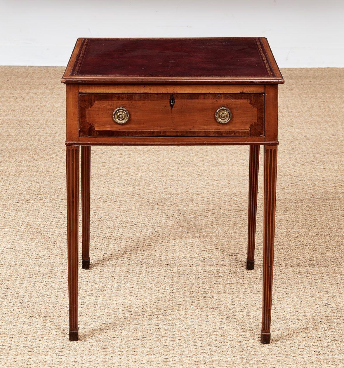 A Sheraton occasional table, circa 1795, in vividly grained satinwood with rosewood cross-banding, having a square top inset with gilt tooled leather, over four drawers, one to each side with three being dummy drawers, each with a pair of bronze