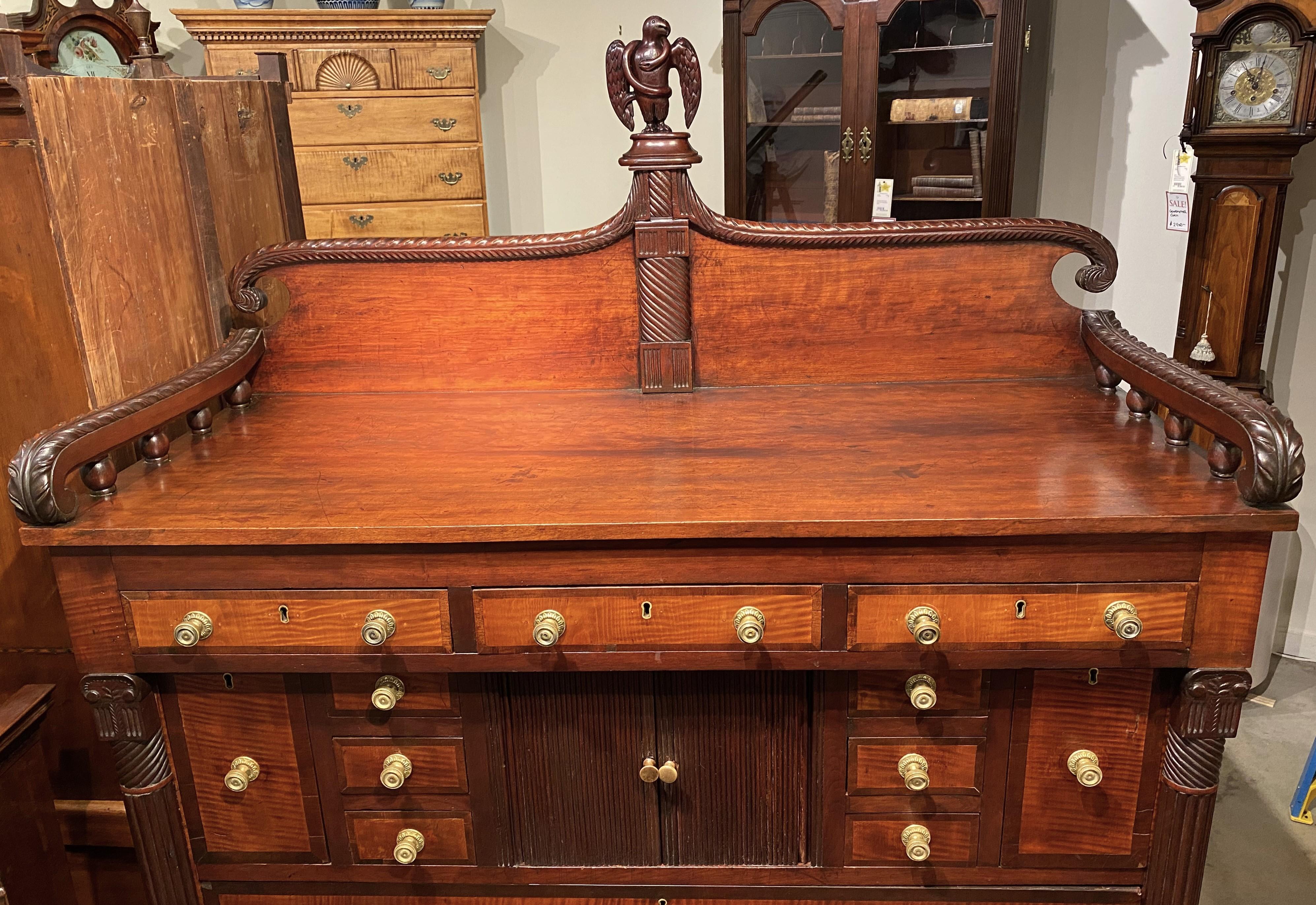 An impressive Sheraton mahogany and tiger maple tall chest or server with a scrolled feather carved wooden gallery with central eagle and serpent finial surmounting a case with three fitted small drawers over a central tambour door, opening to a