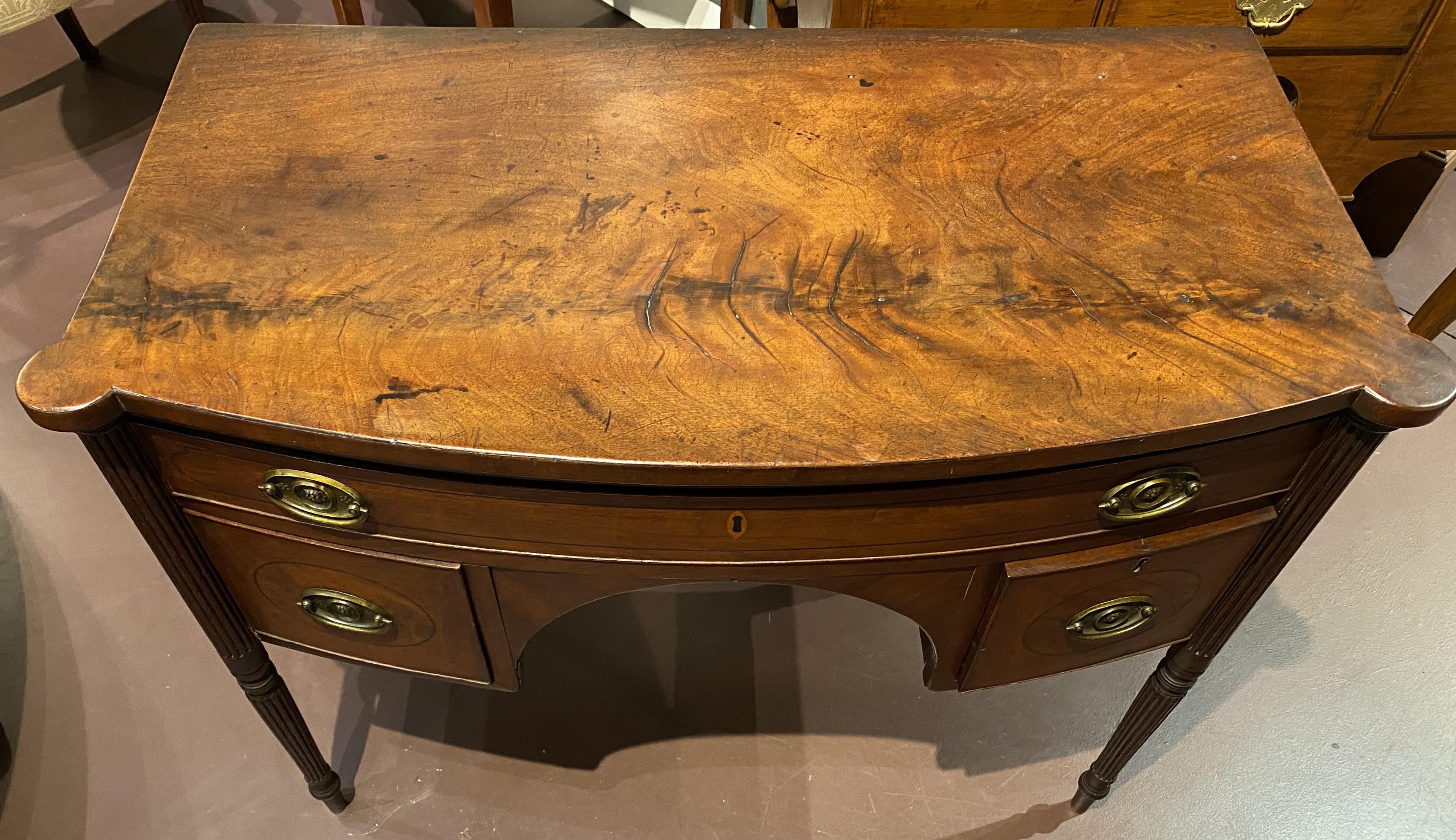 A fine Sheraton crotched mahogany bow front dressing table or server with conforming top with turret corners, surmounting a case with single long drawer over two fitted drawers flanking an arched kneehole, all with line inlay and oval foliate