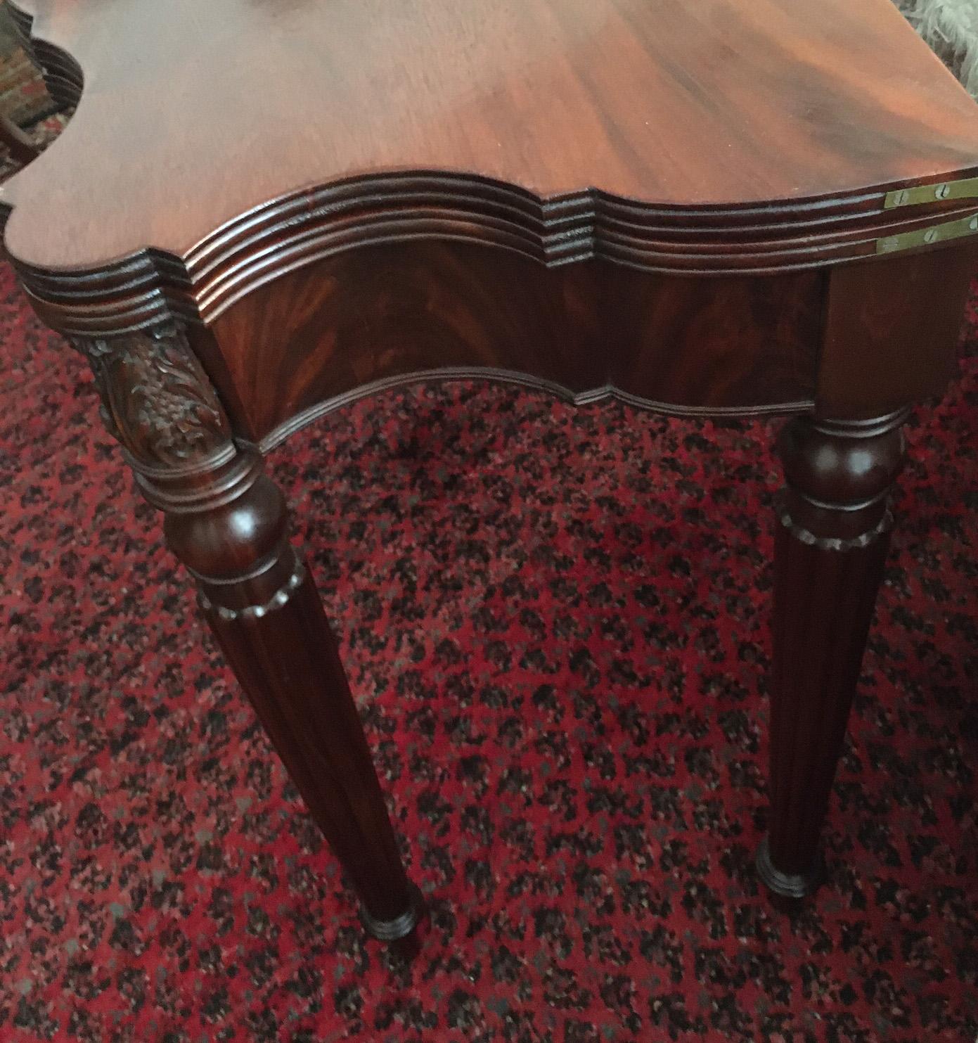 This handsome Sheraton swing leg game table offers mahogany construction with a flip top. Features include turned reeded legs ending in circular end cap, carved acanthus tops in front and beautifully carved serpentine front top and sides. Gorgeous