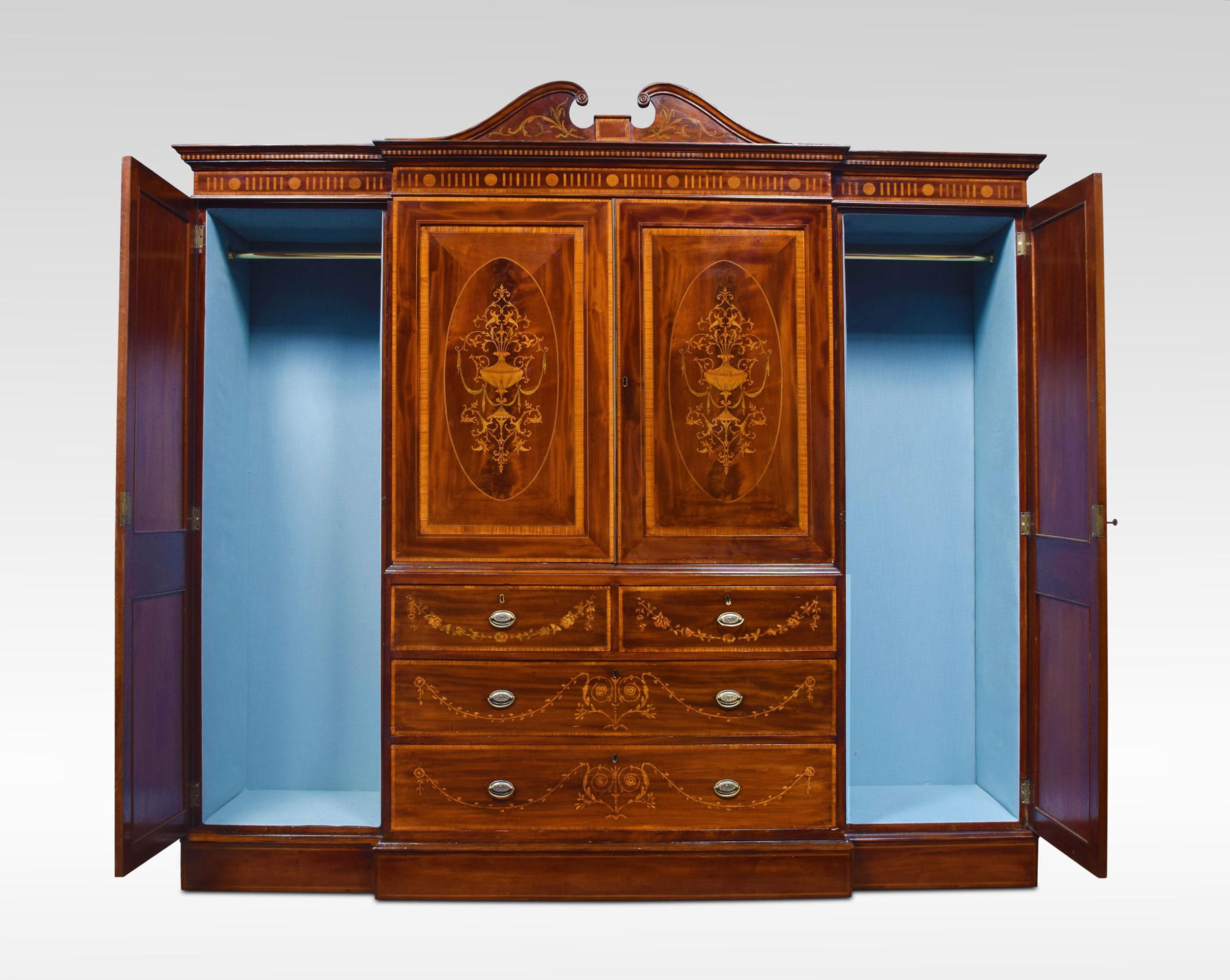 Sheraton revival mahogany satinwood crossbanded boxwood and ebony strung and inlaid breakfront wardrobe. The swan neck pediment above a moulded cornice inlaid with rosettes. The two centre doors opening to reveal the upholstered interior and hanging