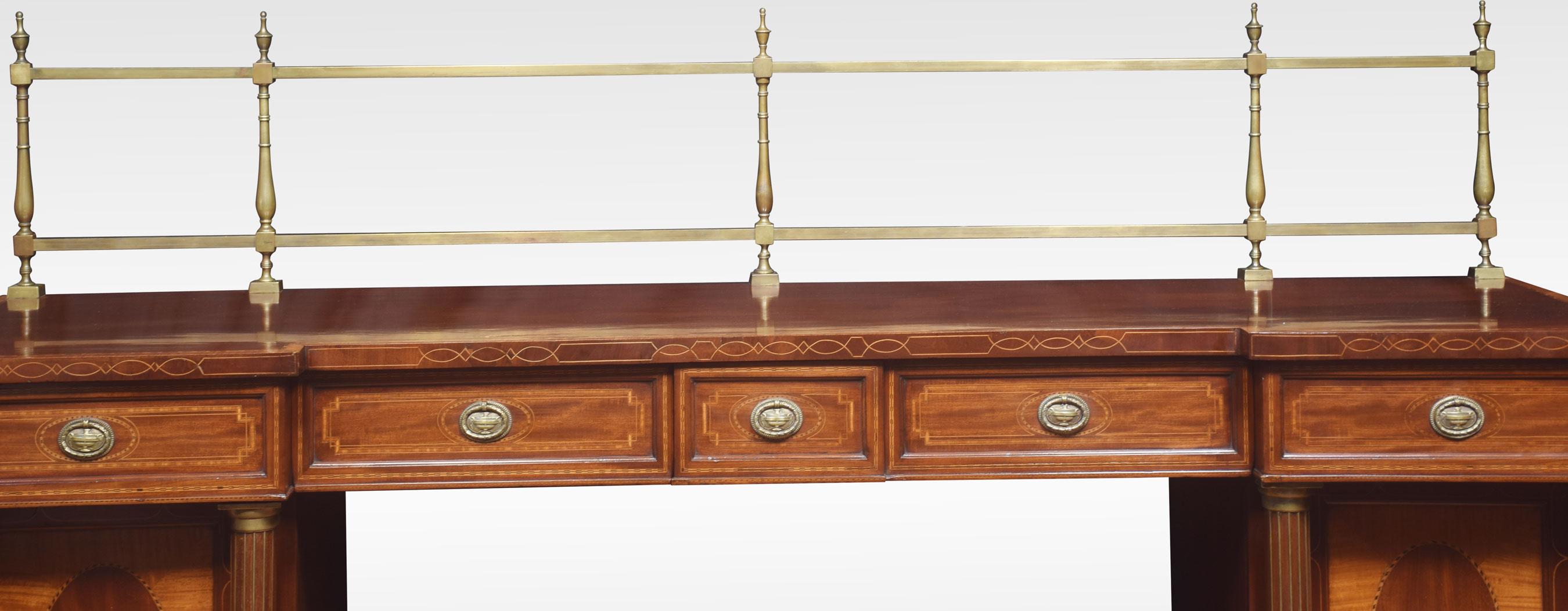 Sheraton revival mahogany inlaid sideboard. The raised brass gallery back above large mahogany inverted breakfront top with satinwood crossbanded edge to the frieze fitted with an arrangement of drawers all having brass tooled handles. All raised up