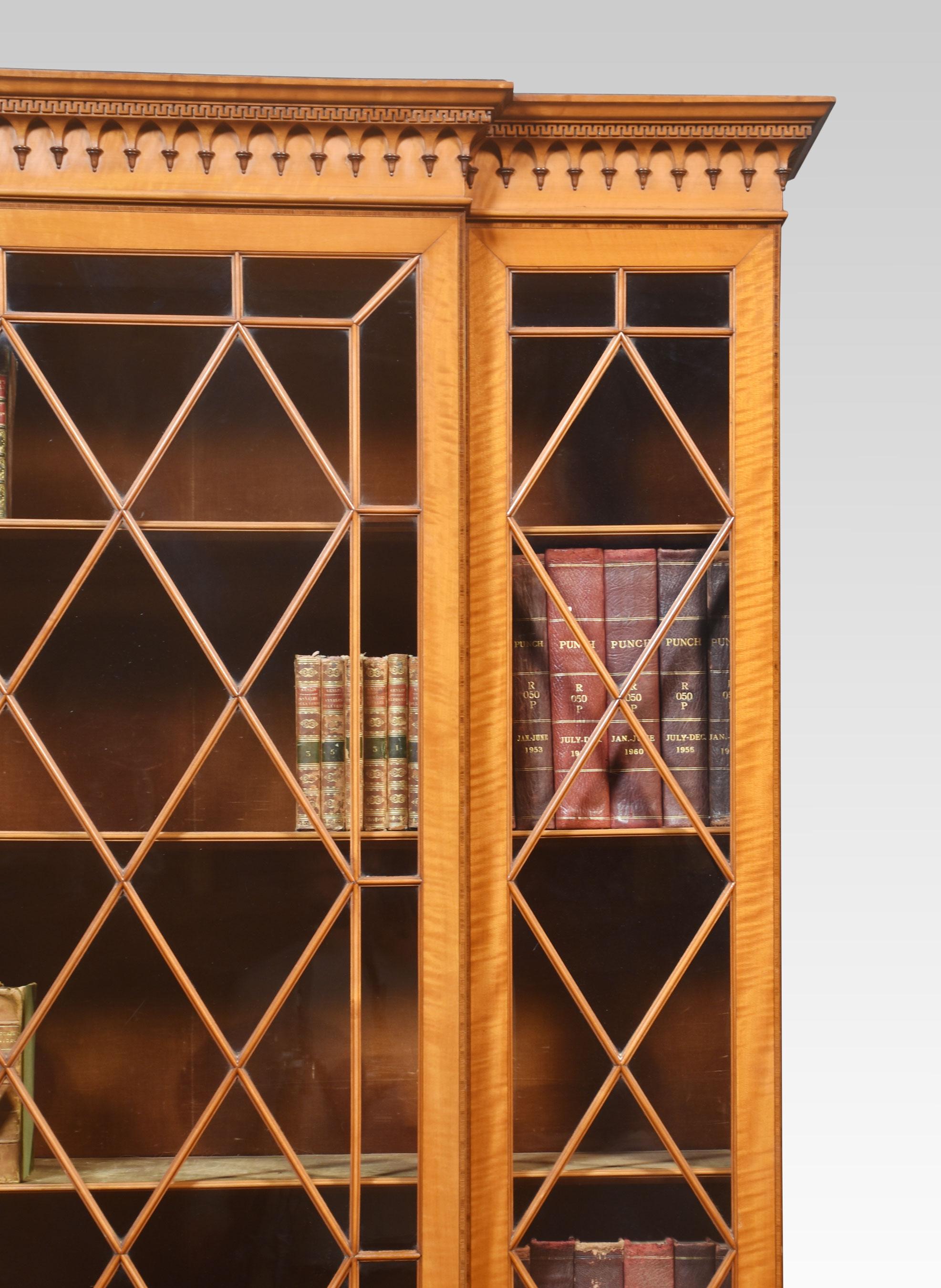 Sheraton revival satinwood cabinet, the carved moulded cornice above large central astragal glazed doors flanked by two further glazed panels. The central door opens to reveal upholstered ajustable shelved interior.
The base section having a