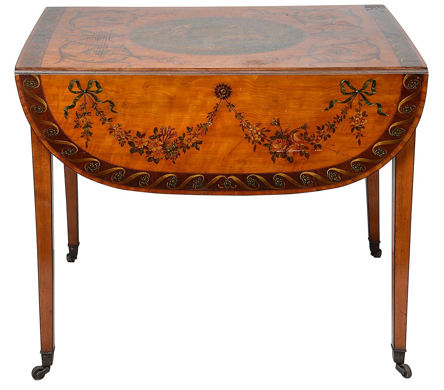 Table Pembroke en bois satiné, de style Sheraton, magnifiquement décorée d'une scène classique au centre et de magnifiques rinceaux de feuillage tout autour. Un seul tiroir en frise et des pieds fuselés carrés, terminés par des roulettes à godets en