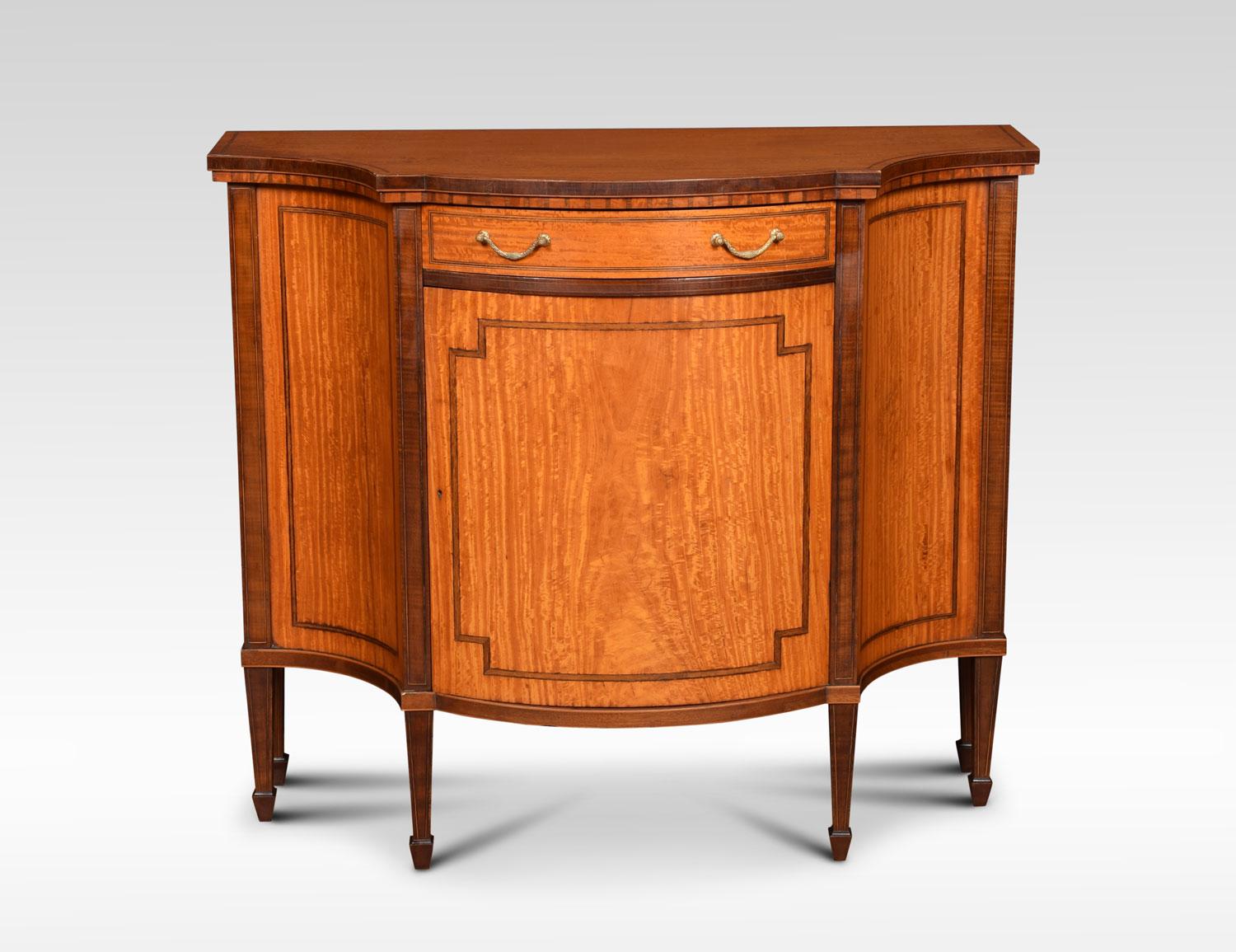 Sheraton Revival inlaid cabinet, the serpentine top above central draw with brass tooled handles. Having large satinwood bowed door below opening to reveal single fixed shelf. All raised up on string inlaid tapering legs and spade