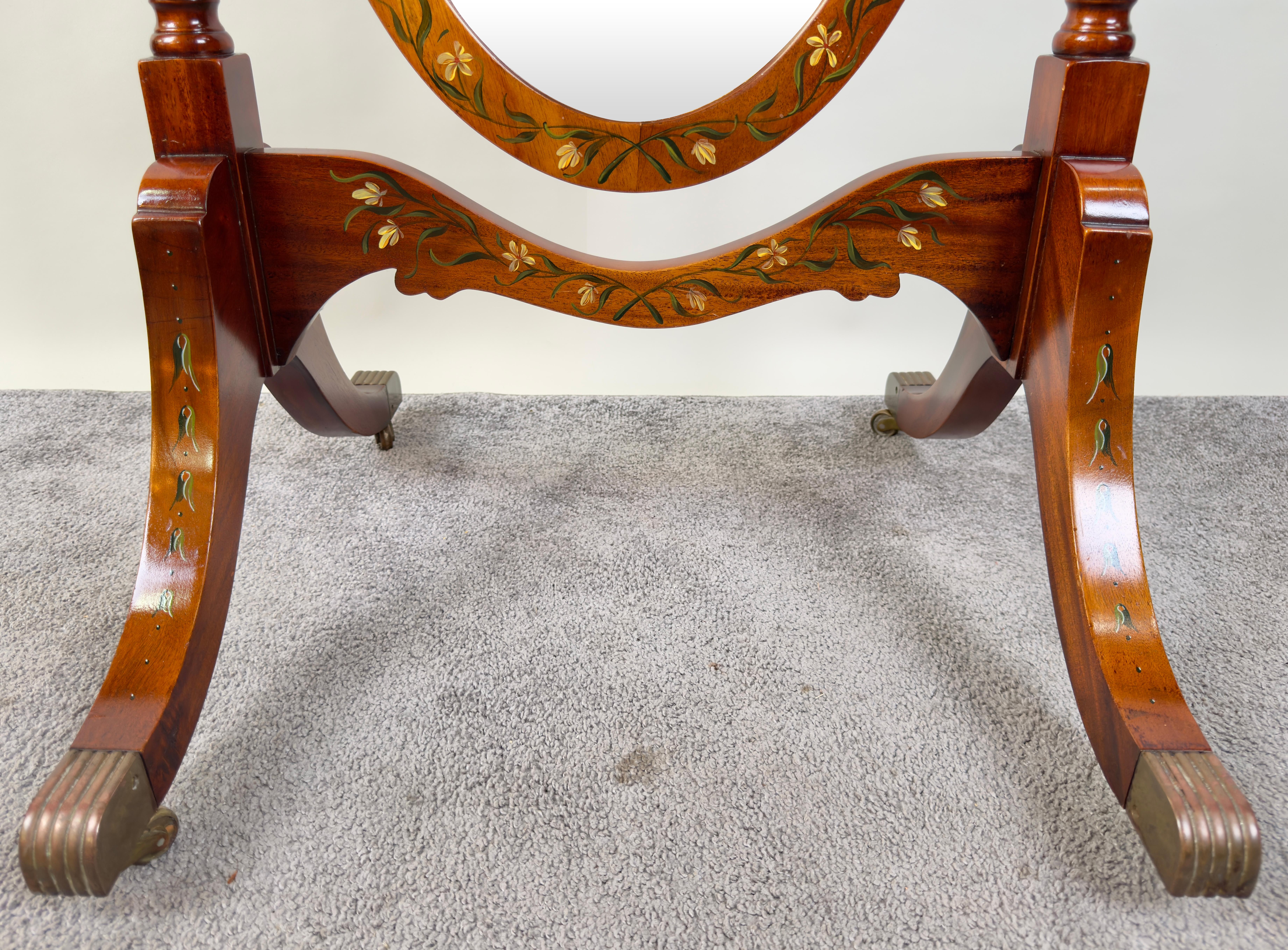 Uno squisito specchio ovale Sheraton Revival, magistralmente realizzato in mogano di alta qualità. L'elegante cornice è ornata da un intricato motivo floreale dipinto a mano nei toni del giallo e del verde, che riflette un'eccezionale attenzione ai