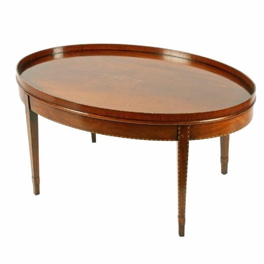 A 20th century Georgian Sheraton style oval mahogany coffee table.

The table has an oval top with a raised gallery and stands on four tapering legs with socks to the tip.

The gallery edge, legs and frieze are all decorated with a chequered