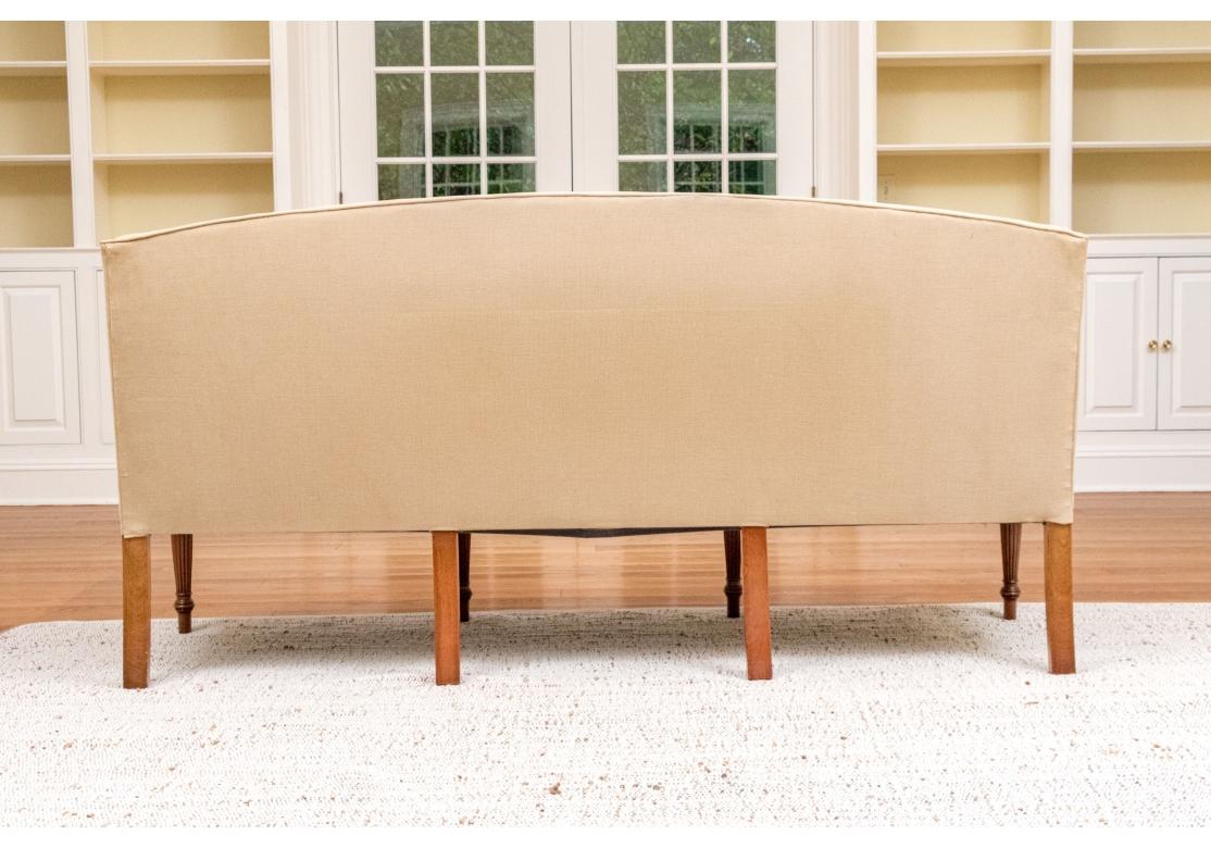 Sheraton style custom upholstered sofa with a single removable seat cushion held by double metal fasteners. The sofa with swan form arms having burl inlay panels, string inlay, carved foliate design and fluted tapering legs.The sofa is upholstered
