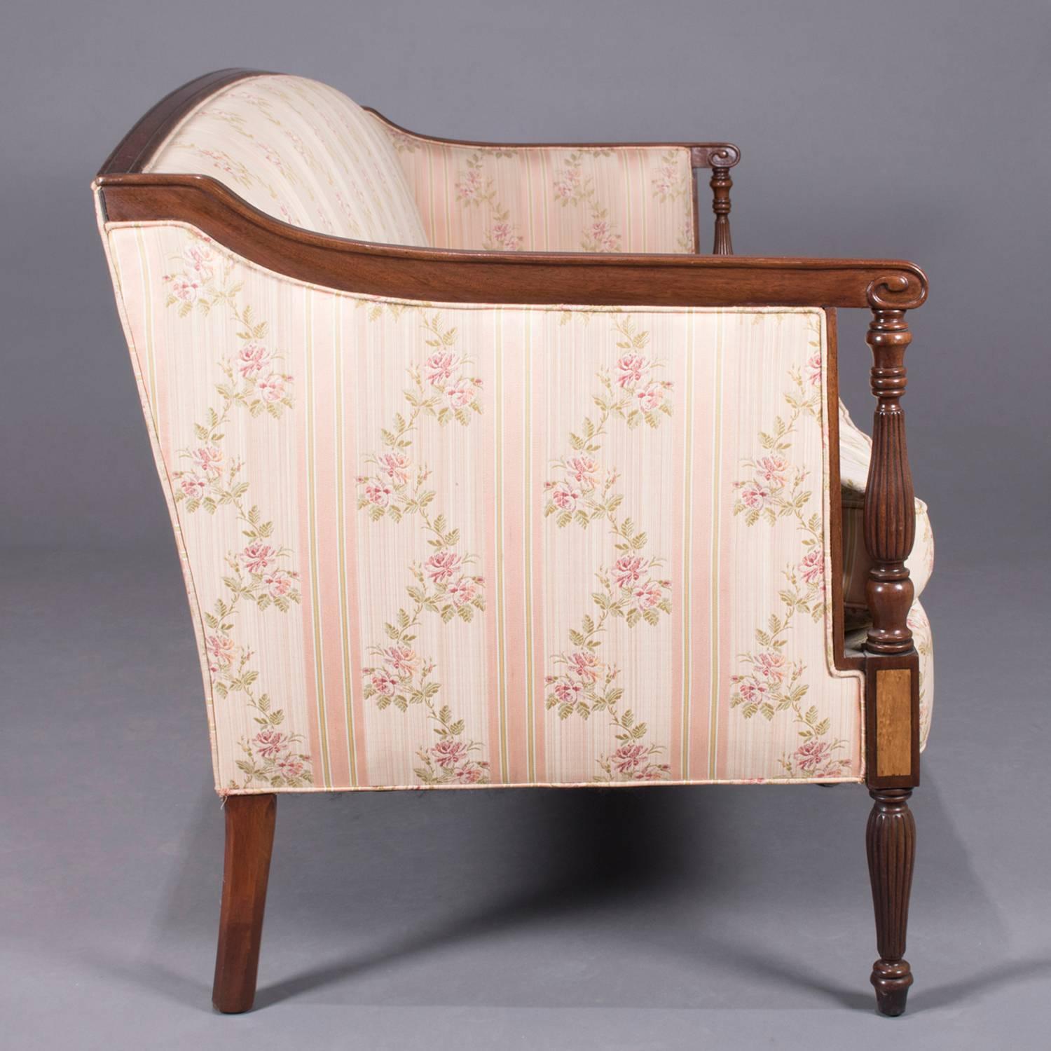 Sheraton School camelback settee by W. & J. Sloan features mahogany frame with carved scroll arms supported by open reeded columns above burl inlay joints and raised on tapered and reeded legs, upholstered and with down filled cushion, maker label